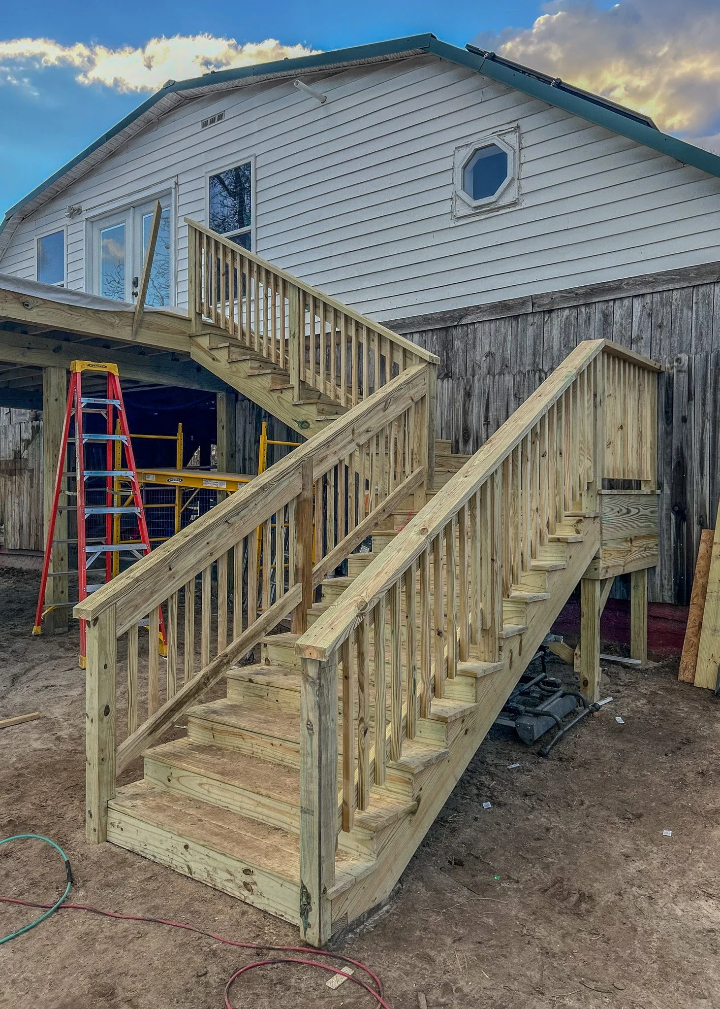 New wooden outdoor staircase under construction attached to a house with white and weathered wood siding.