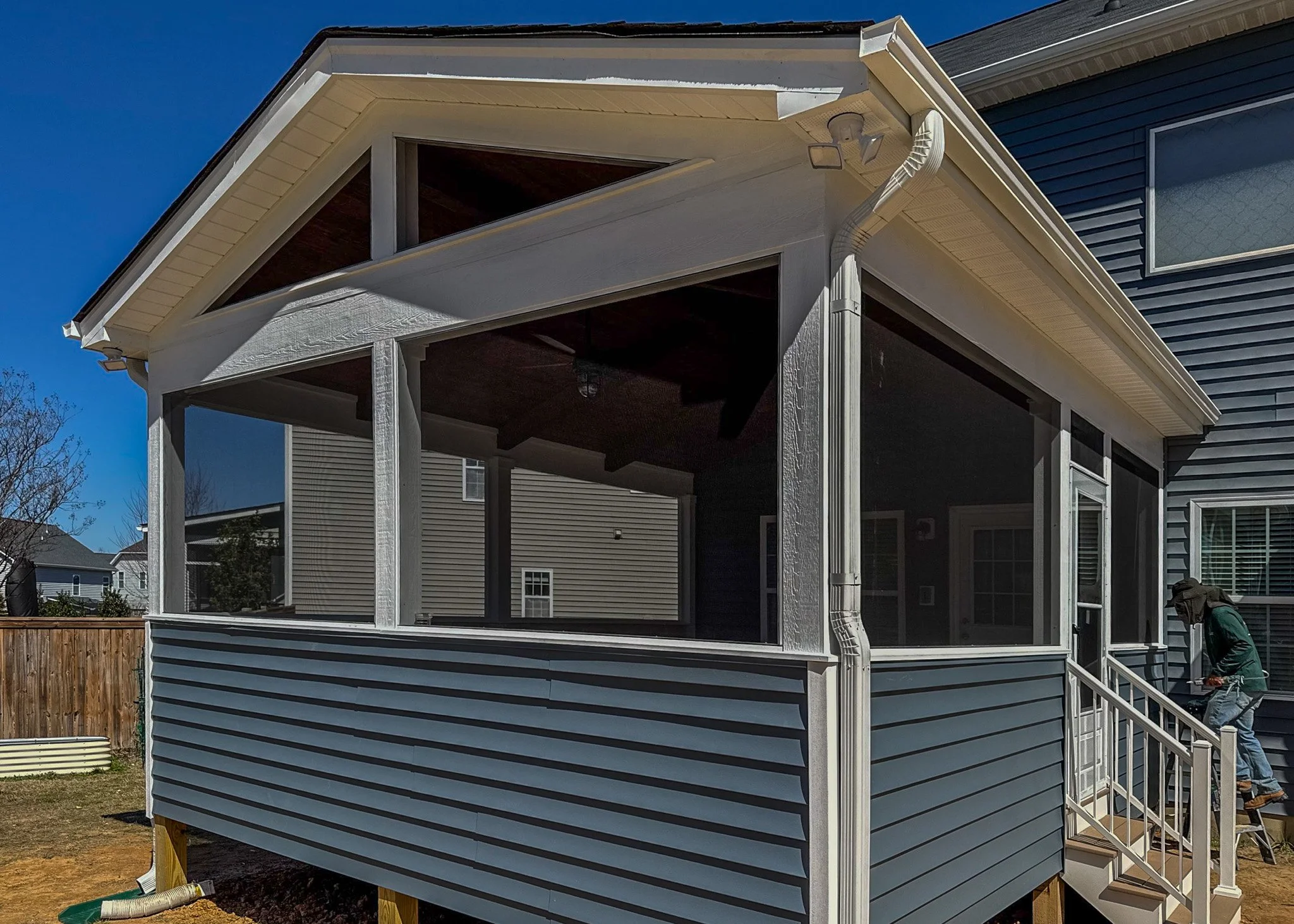 Newly built screened porch attached to a blue house on a sunny day with a person working on the stairs.