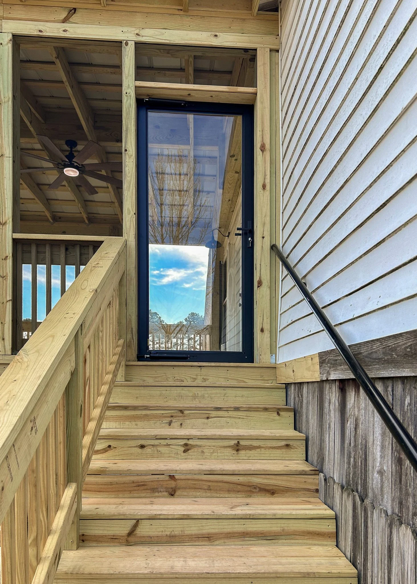 Wooden stairs leading to a glass door on the porch of a house under construction.