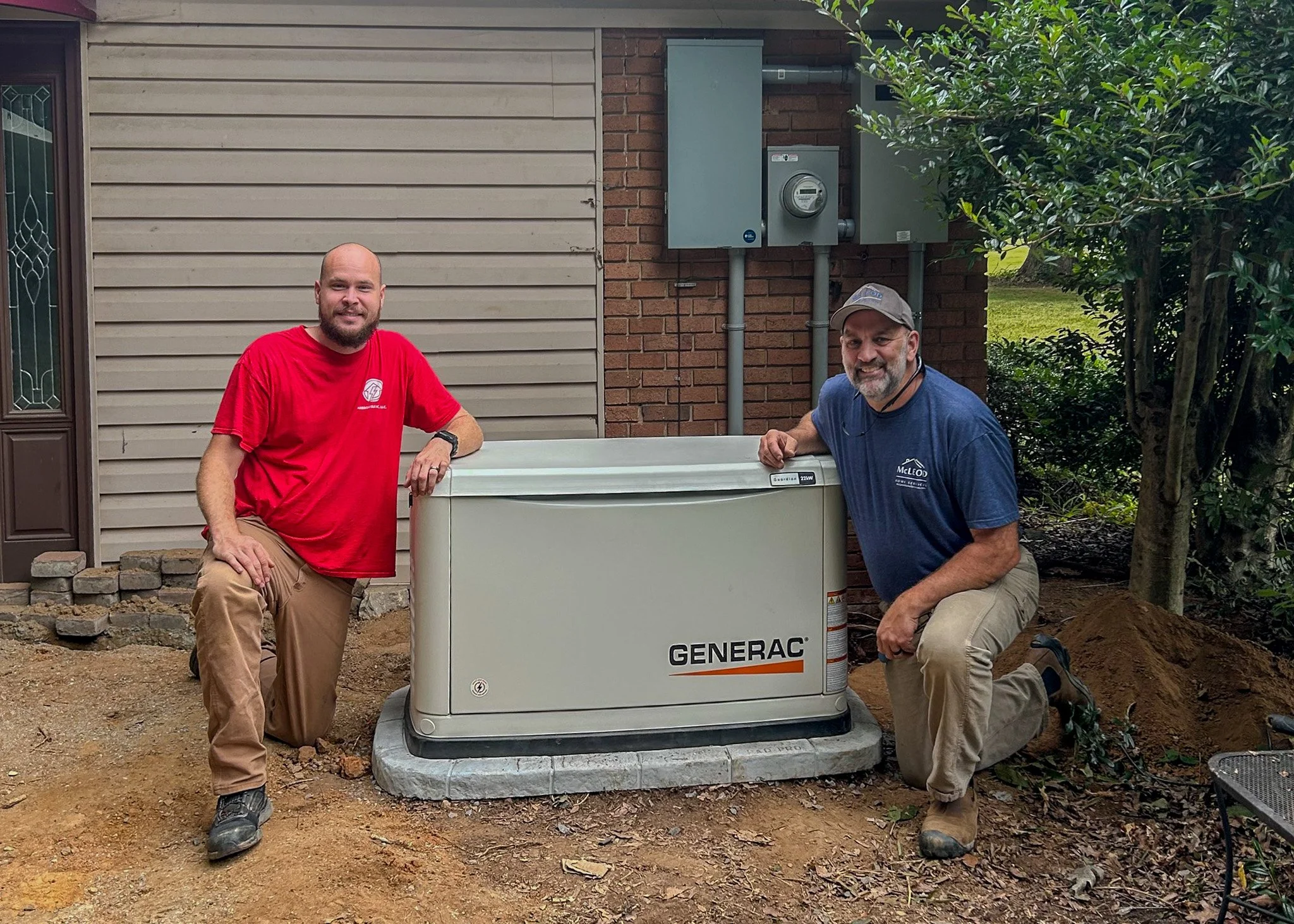 Two men kneeling beside a Generac generator outside a house, with one in a red shirt and the other in a blue shirt and a cap.