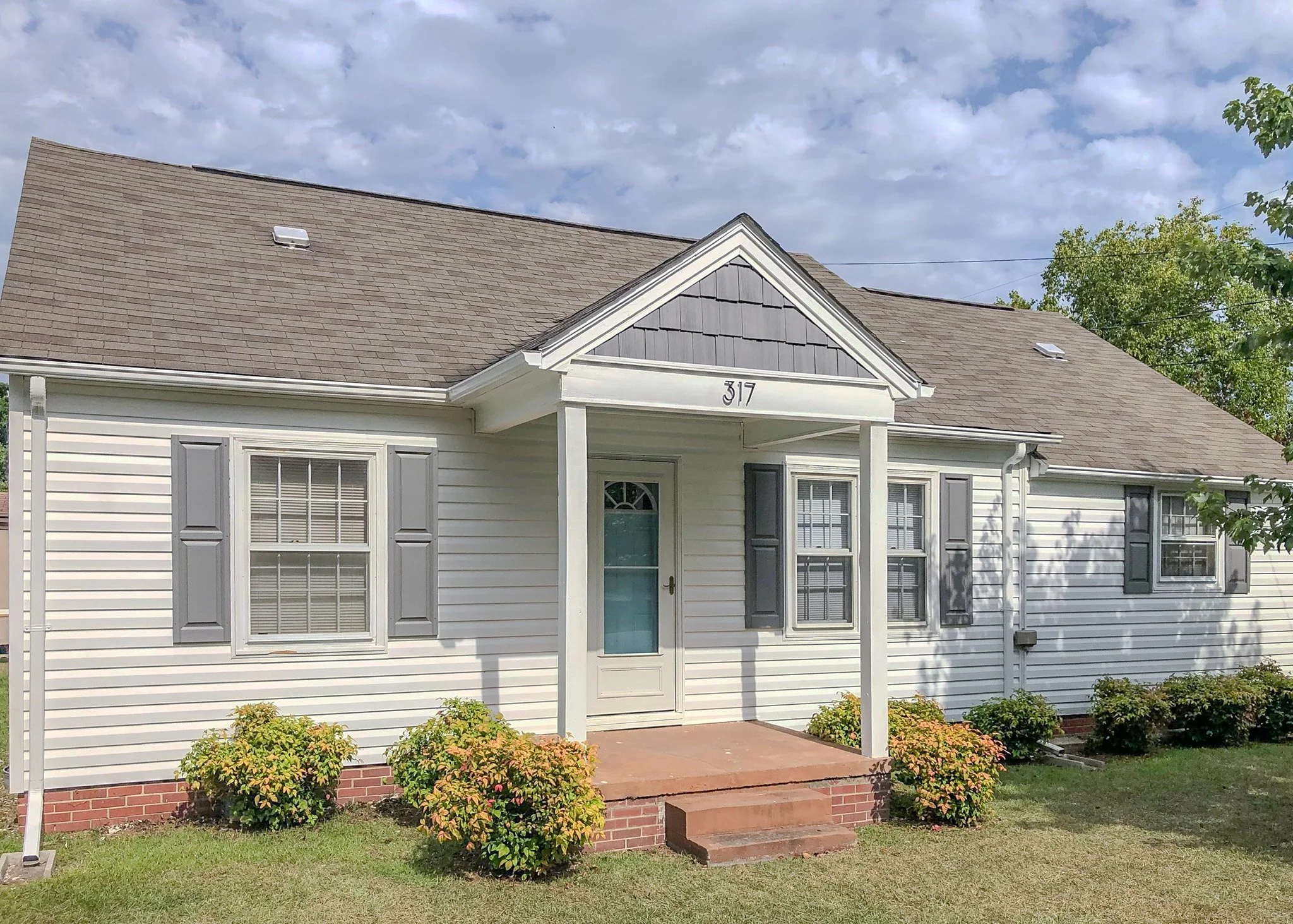 White house with gray shutters, brick steps, and a small porch under a cloudy sky.