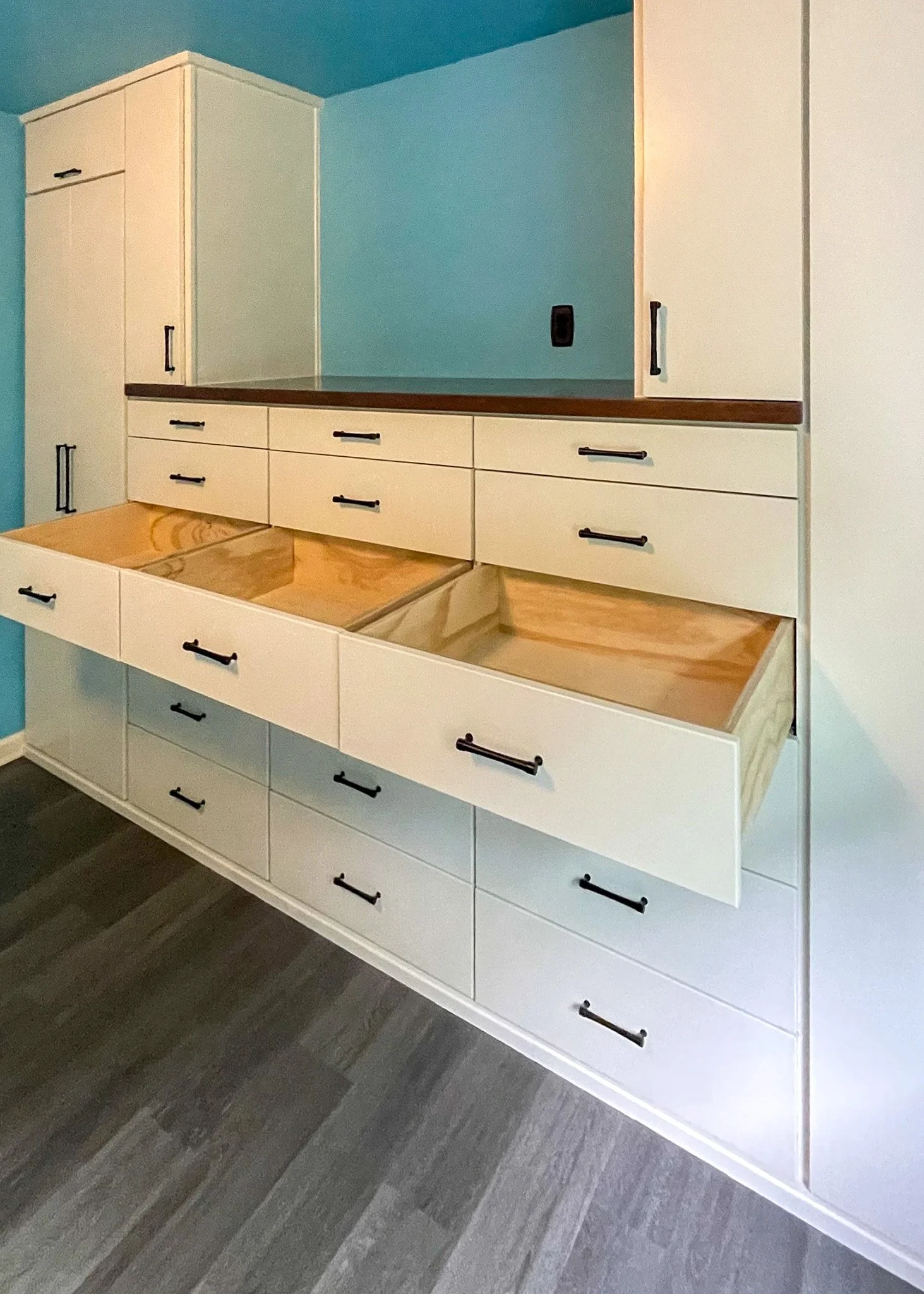 A kitchen cabinet installation in progress with open drawers and a backsplash area, featuring white cabinets with black handles and a wooden countertop.