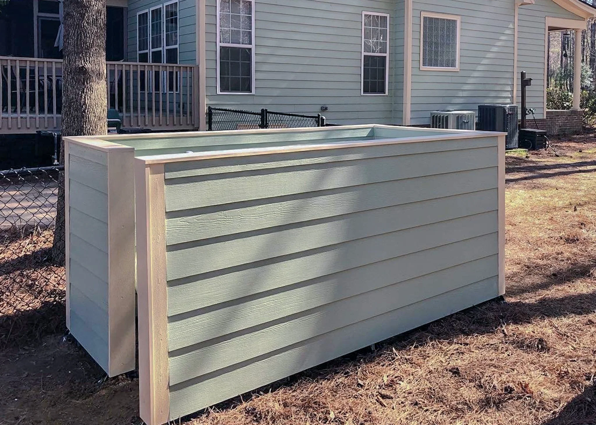 Backyard scene with a house, a wooden raised garden bed, trees, and a wire fence.