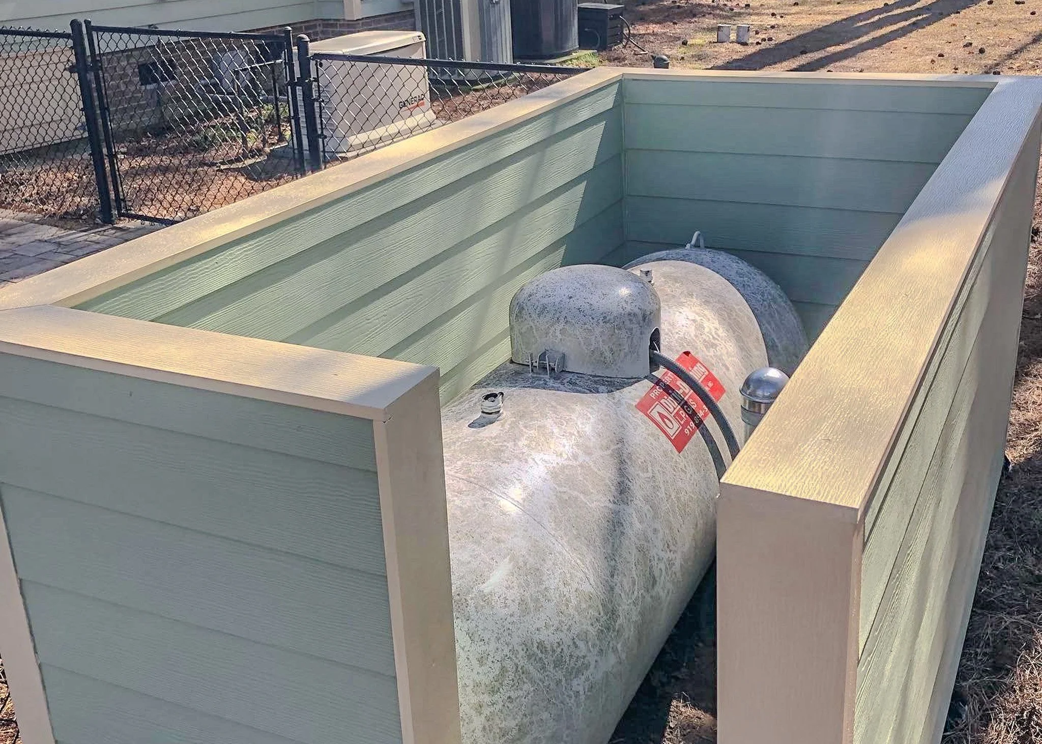 A large cylindrical propane tank installed inside a wooden enclosure in an outdoor area.