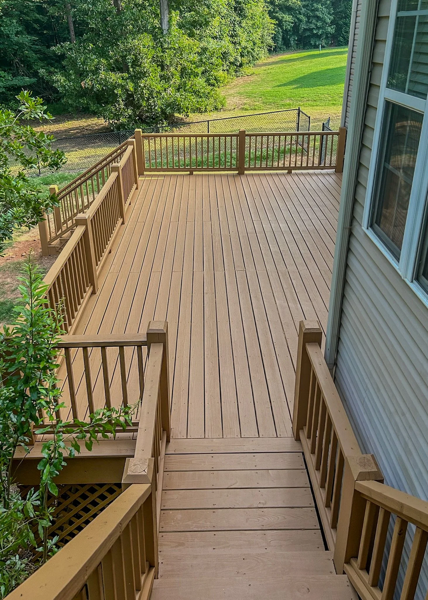 Wooden backyard deck with a railing, overlooking a grassy yard with trees.