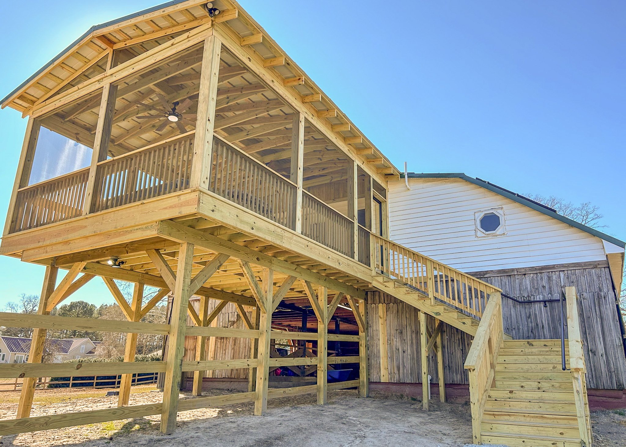 A second-story wooden deck with railings and stairs attached to a house, under construction, with blue sky in background.