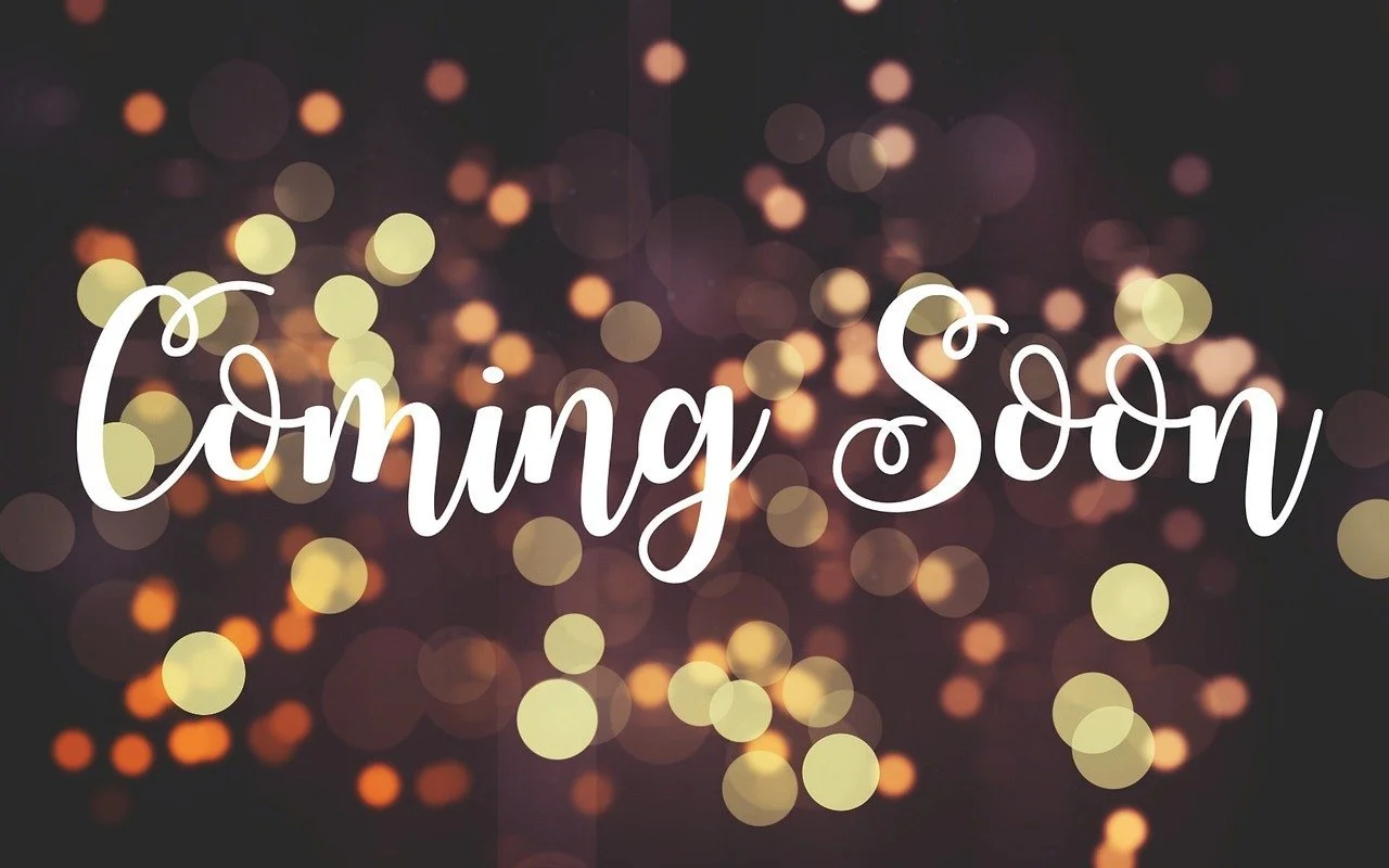 An image with the words Coming Soon with a blurred background of white and gold festive lights.