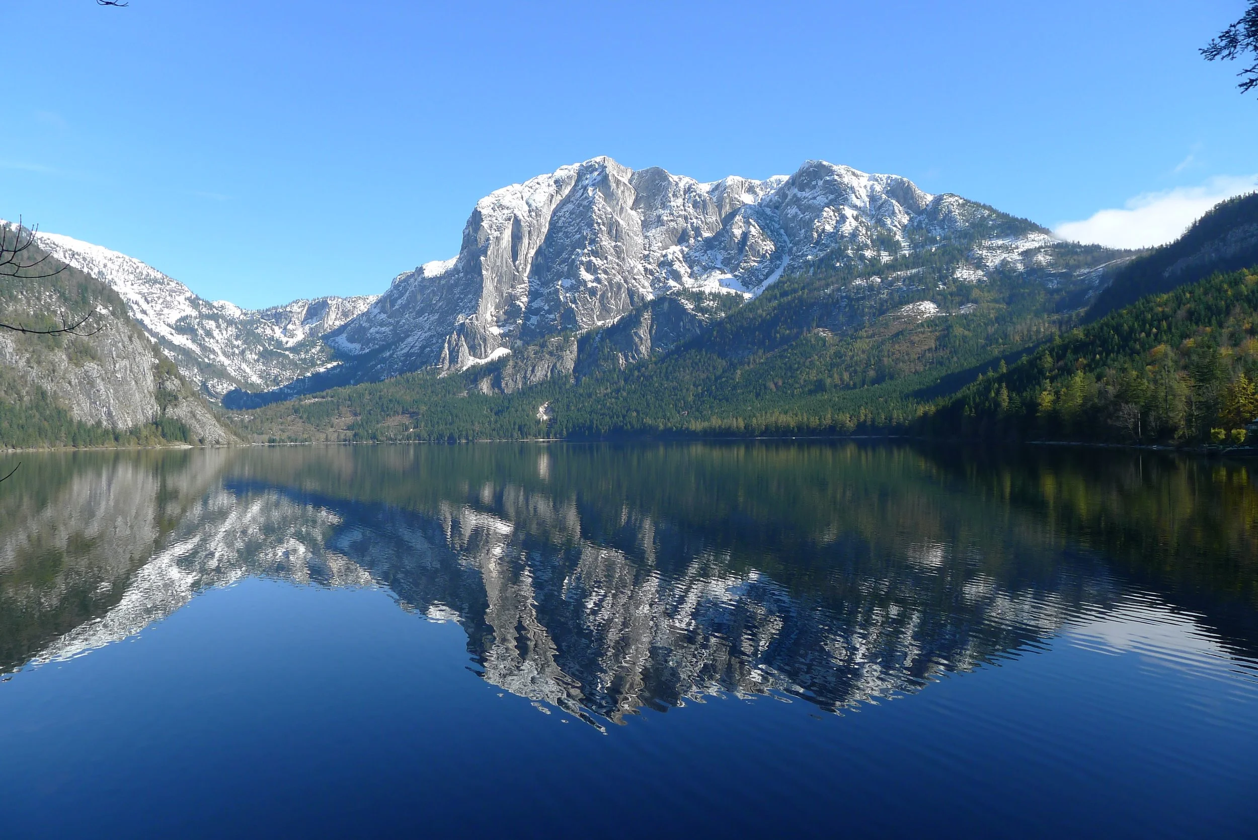 Snow-covered mountains reflecting in a lake under a clear blue sky.