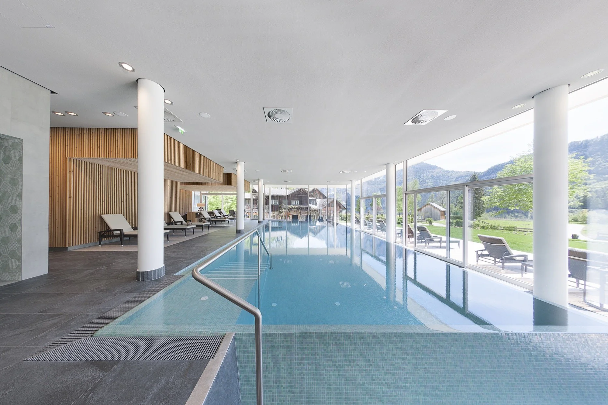 Indoor swimming pool with lounge chairs and large windows overlooking a scenic outdoor landscape.