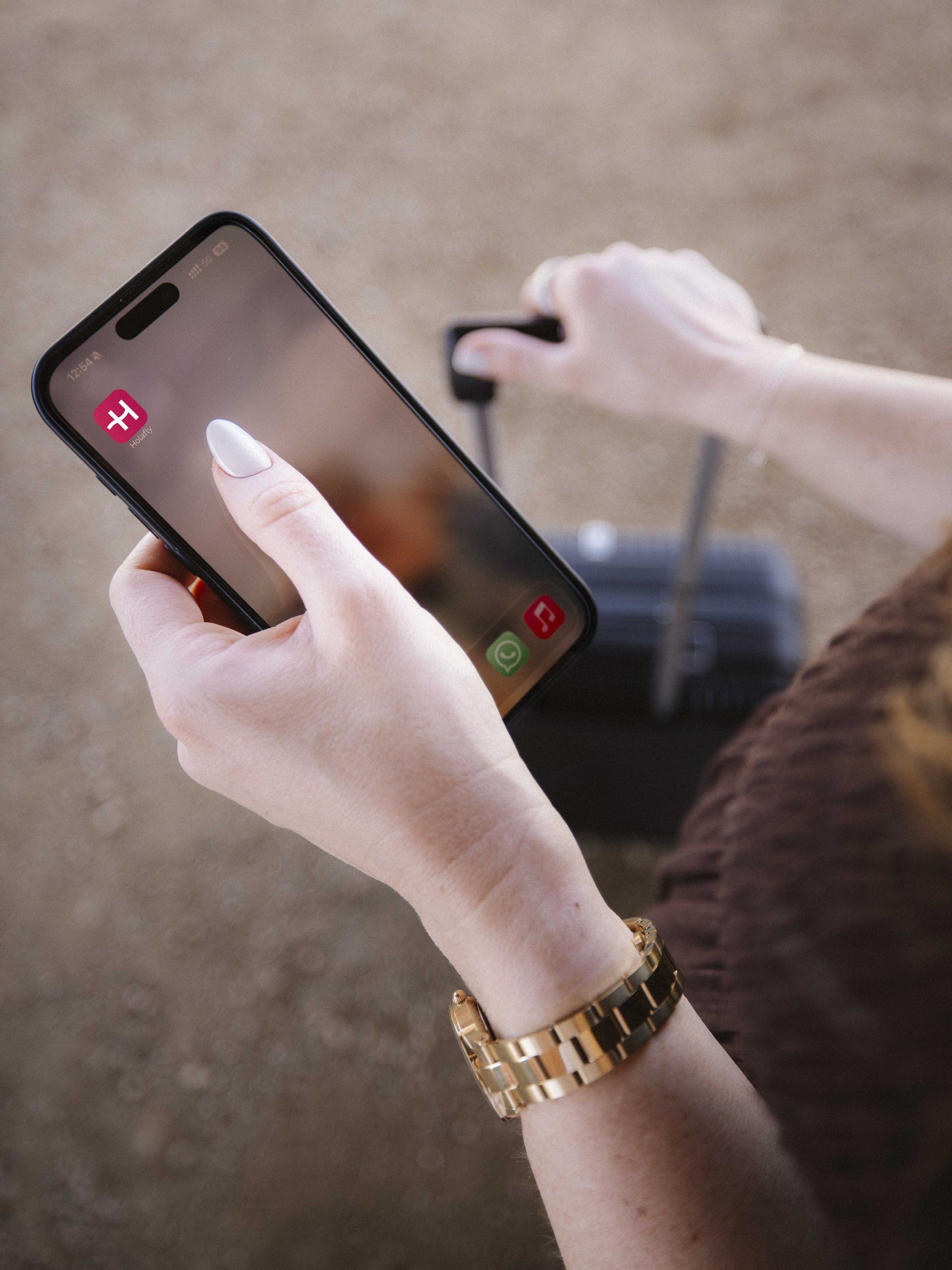 A person holding a smartphone and pulling a carry-on suitcase, with apps visible on the phone's screen.