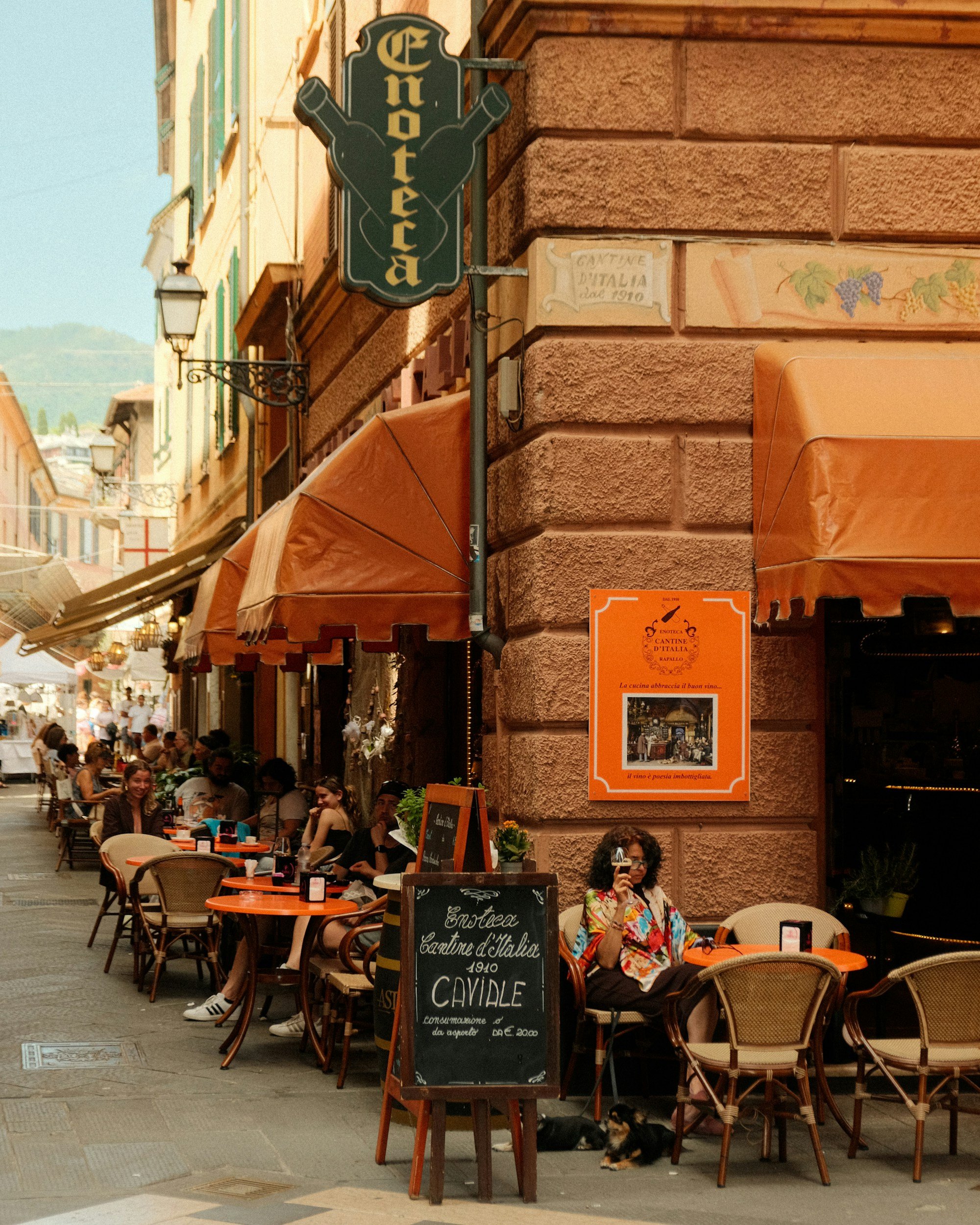 Street scene with a multi-story building housing a restaurant called Miramare, outdoor seating, palm trees, pedestrians, cars, and decorative street lamps under a partly cloudy sky.