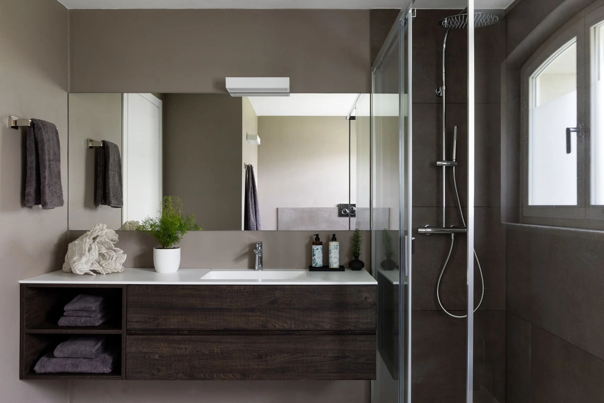 Modern bathroom with a large mirror, dark wood vanity, and a walk-in shower with glass doors and a rainfall showerhead.