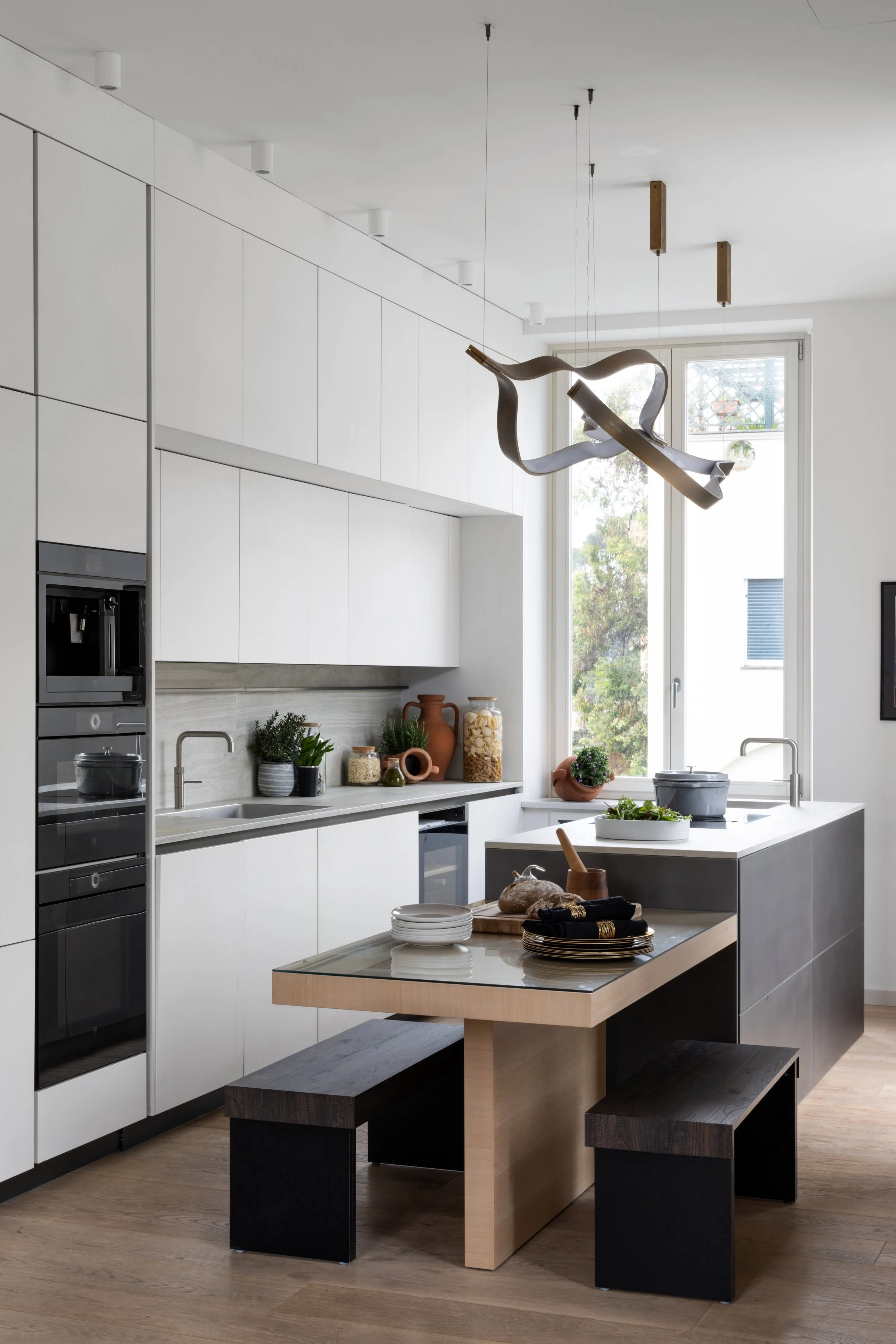 Modern kitchen with white cabinets, a large window, a kitchen island, and black and wooden seating.