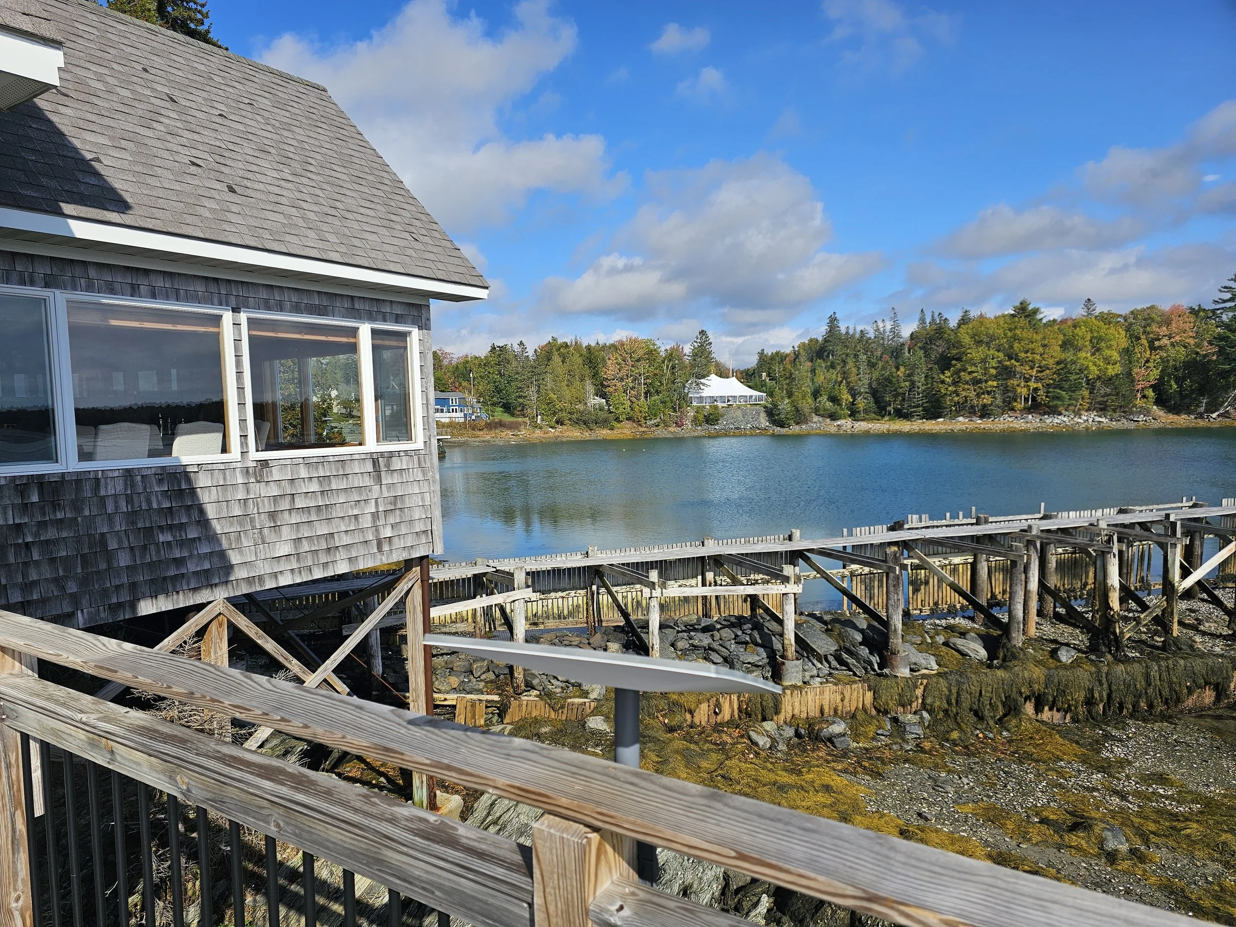 Shingled waterfront building beside a wooden dock at The Foggy Pearl in Hancock, Maine.