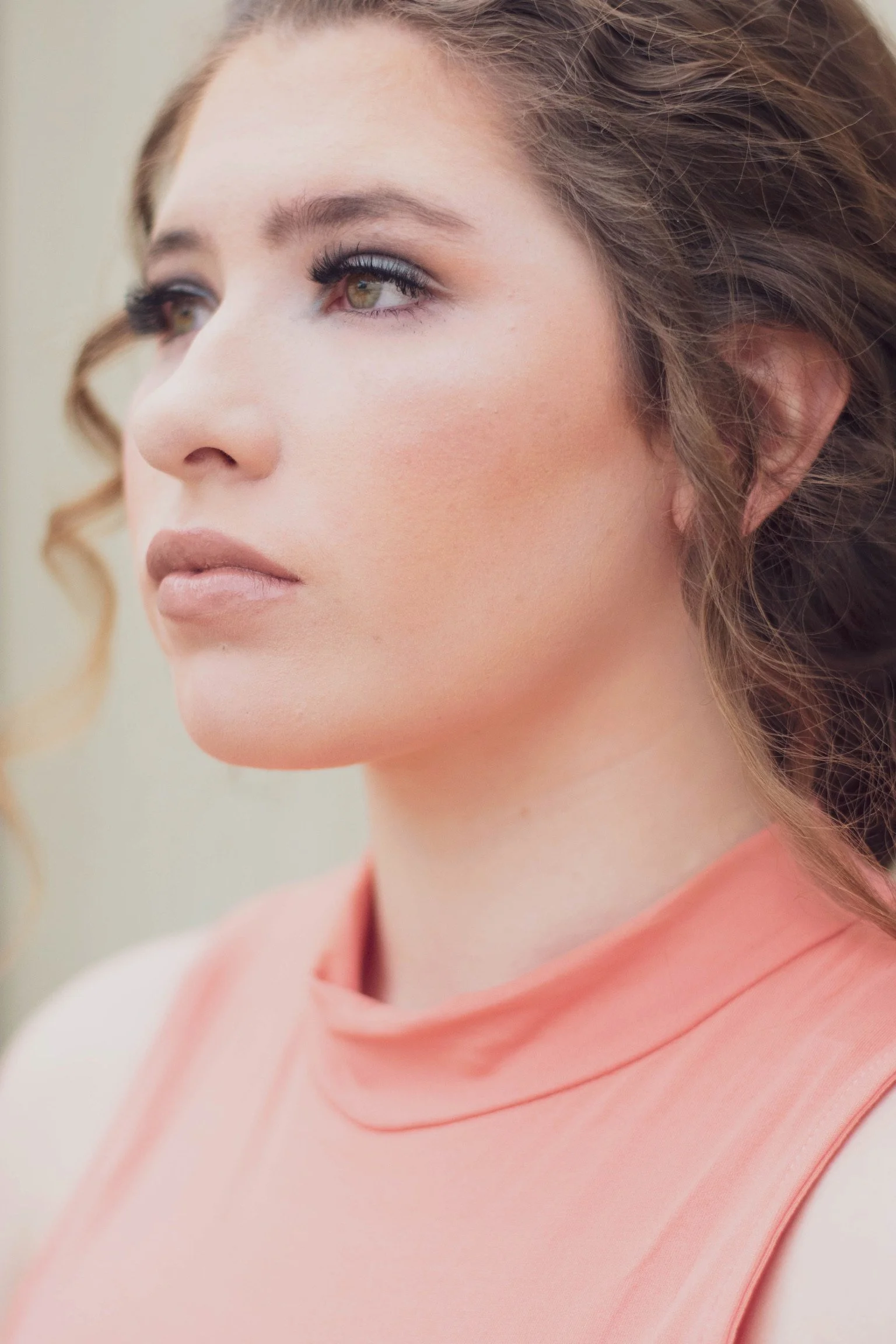 Close-up of a woman with makeup and curly hair wearing a peach-colored sleeveless top.