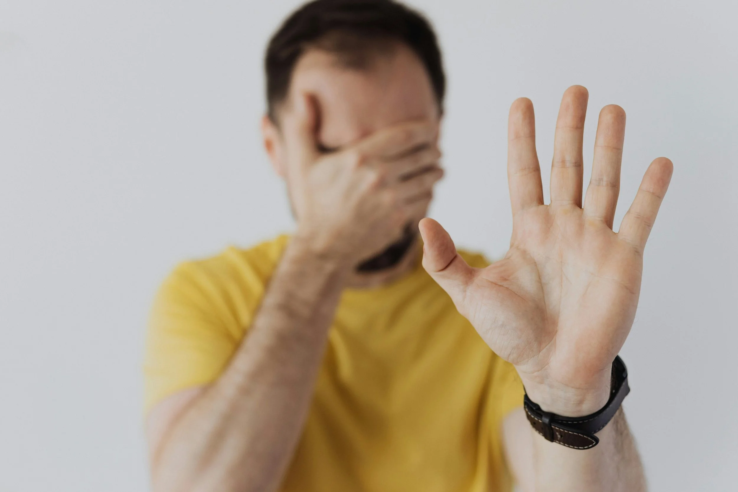 a man covering his eyes, ignoring what emotional avoidance does to long-term mental health