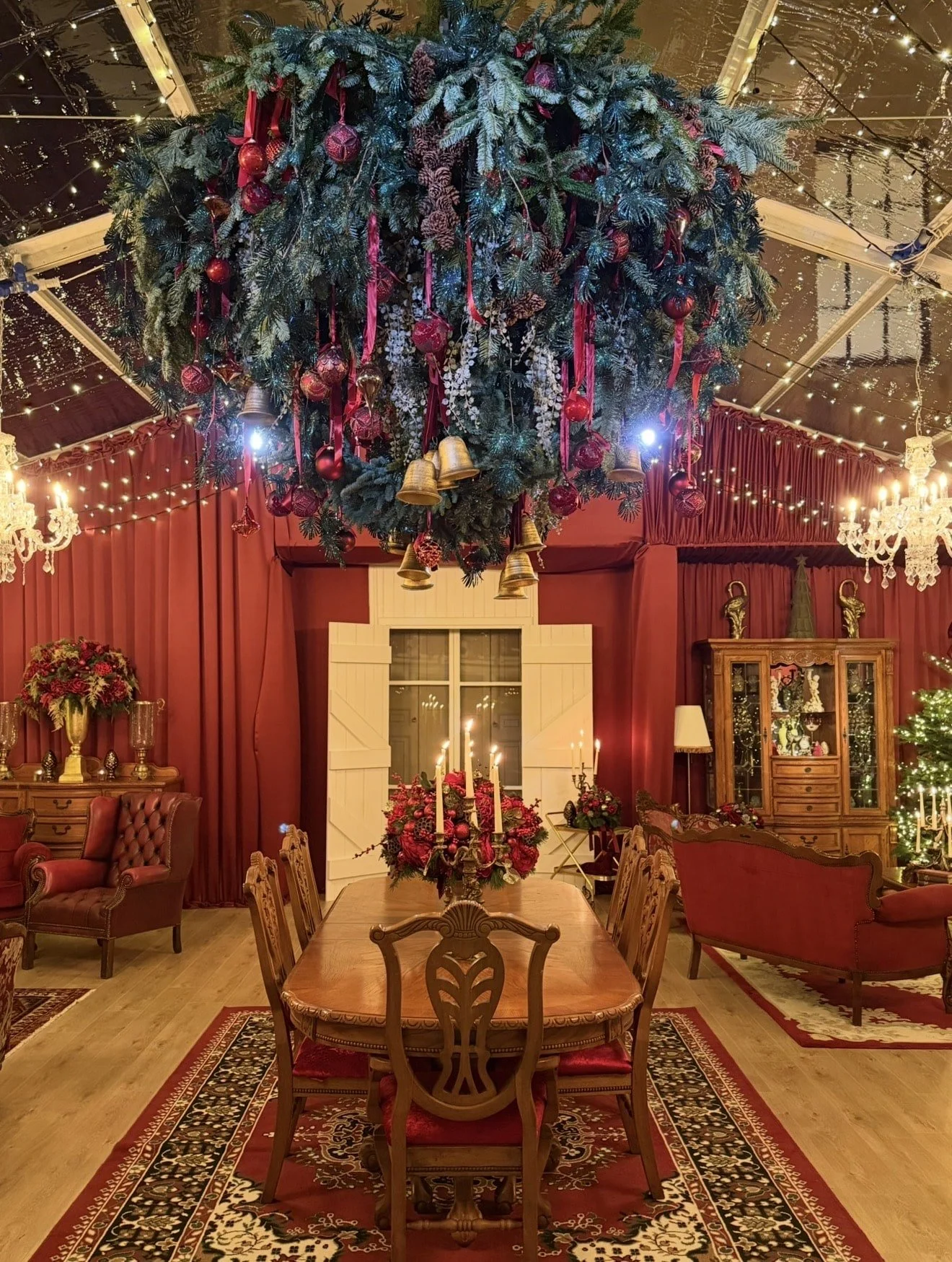 Luxury Christmas dining room installation featuring a dramatic overhead festive display, red floral centrepieces, antique furniture and atmospheric lighting for an immersive setting.
