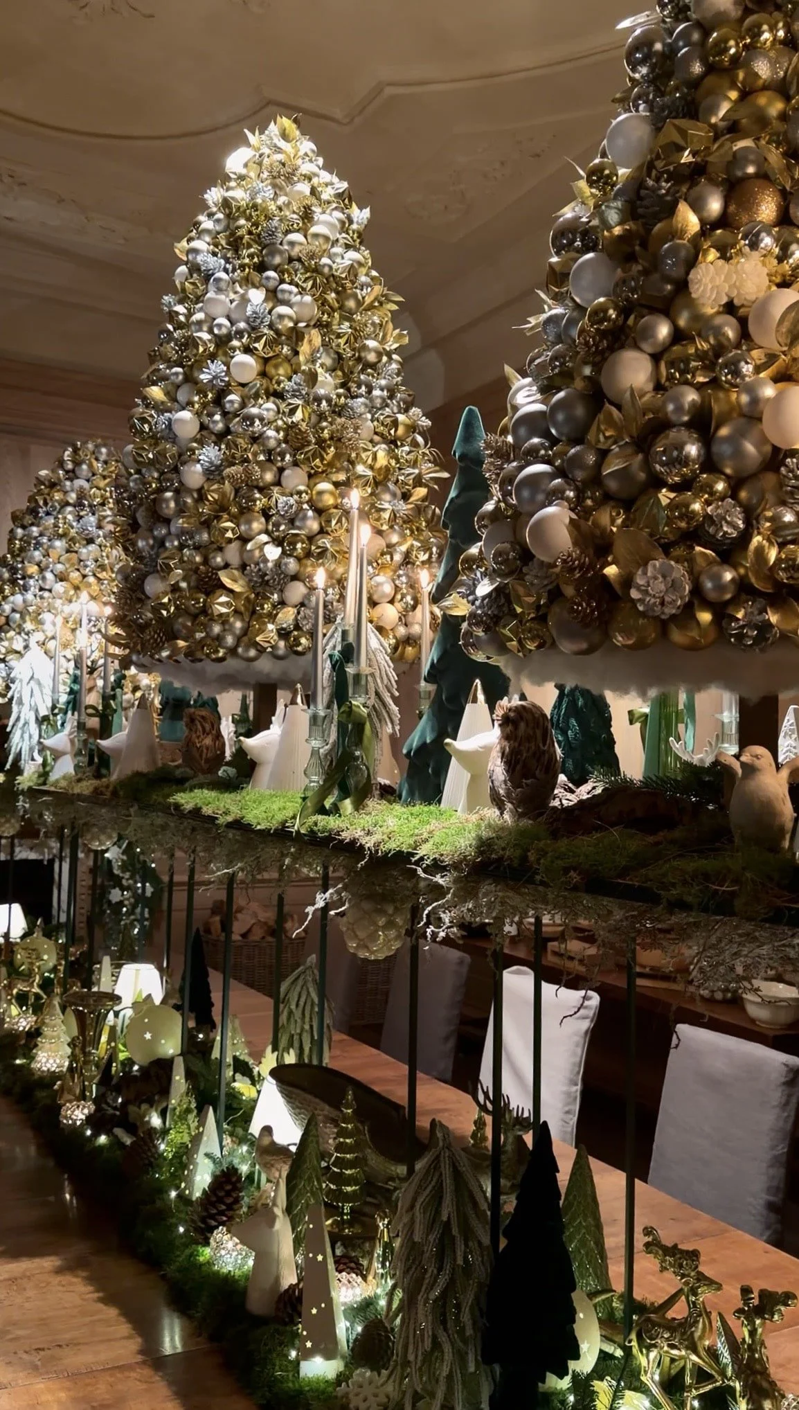 Luxury Christmas tablescape with gold and silver decorative trees, moss detailing, candlelight and woodland-inspired festive décor styled for an elegant seasonal dining experience.