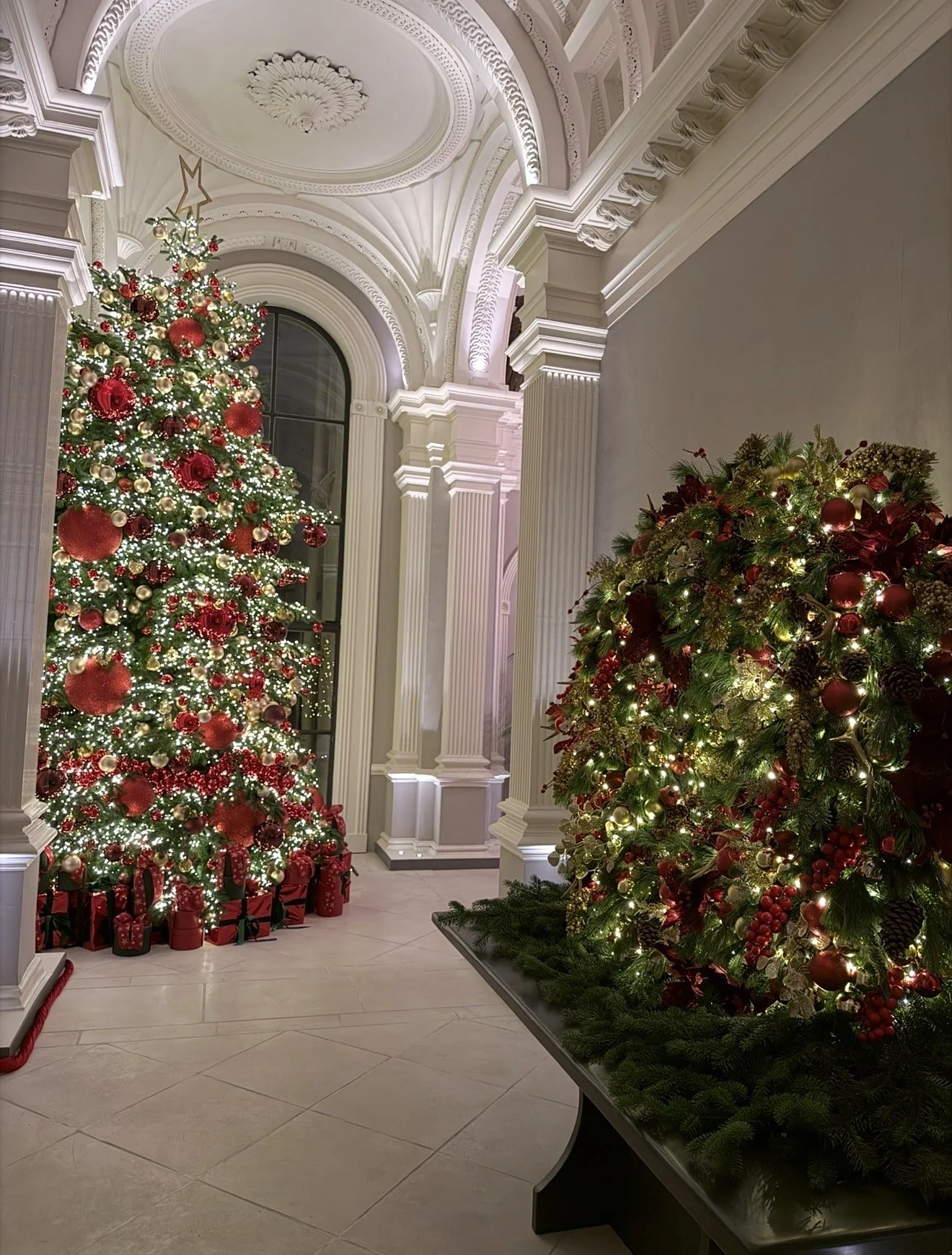 Grand luxury Christmas installation inside a classical interior with illuminated Christmas trees, festive greenery and architectural detailing creating a magical winter atmosphere.