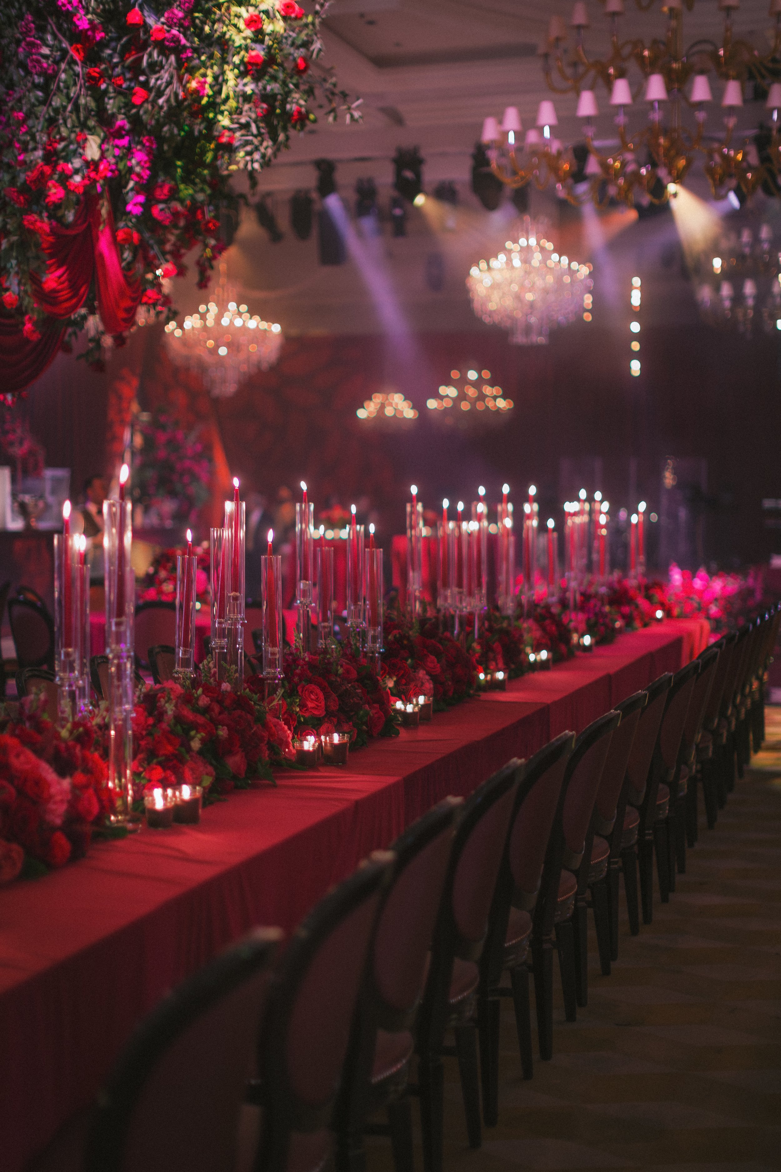 Lavish evening reception filled with red floral canopies, glowing chandeliers and round tables set for an opulent and atmospheric celebration.