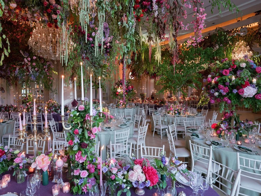 Luxury wedding reception at Adare Manor, Ireland, transformed with spectacular suspended floral installations, cascading greenery, crystal chandeliers and colourful flowers surrounding elegant dining tables.
