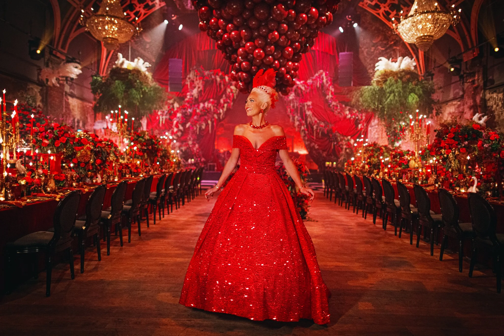 Amie Bone within the immersive floral design of Fantasia 2, surrounded by dramatic red florals, candlelit tablescapes, suspended installations, and luxury event styling designed to create atmosphere and impact.