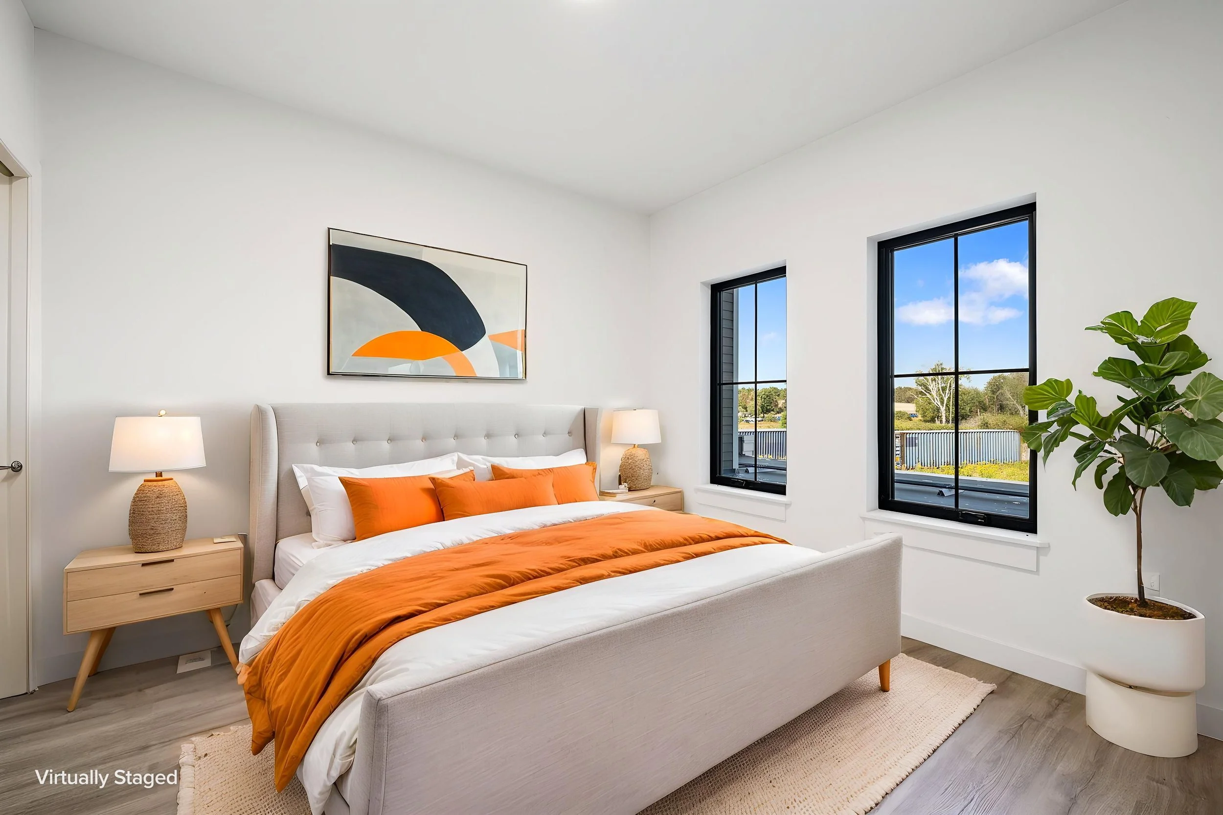 A bedroom with a white upholstered bed, orange bedding, and matching pillows. The Residences at North Harbor on Lake Superior in Marquette Michigan.