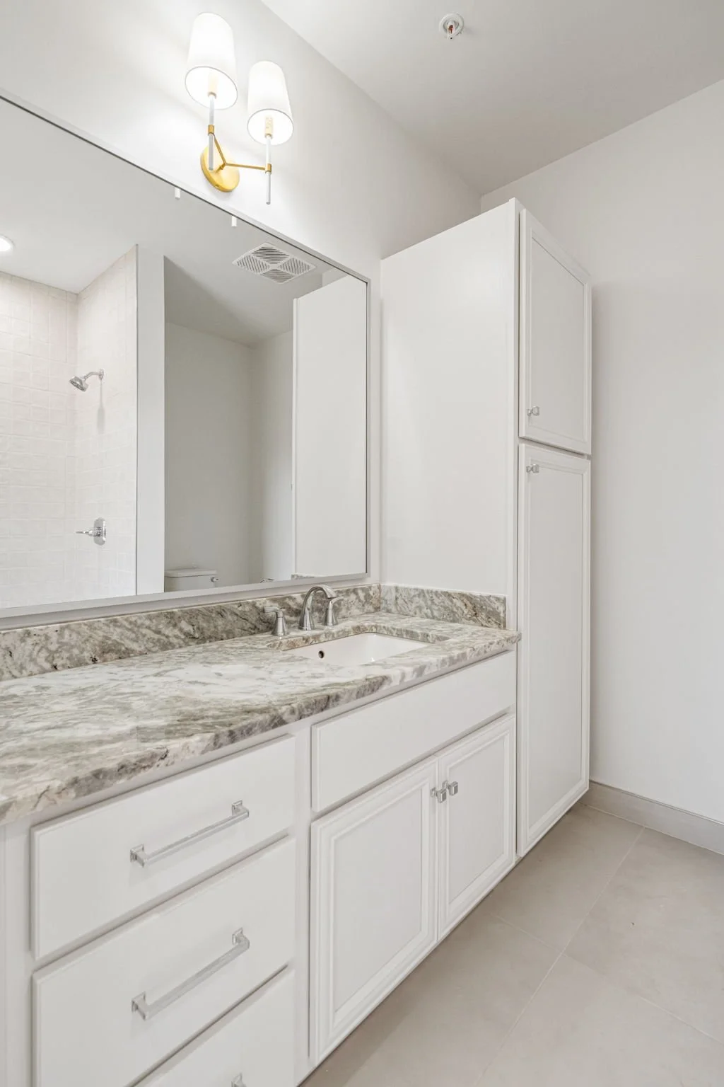 Bathroom vanity with marble countertop, mirror, white cabinets, and a light fixture overhead. The Residences at North Harbor on Lake Superior in Marquette Michigan.