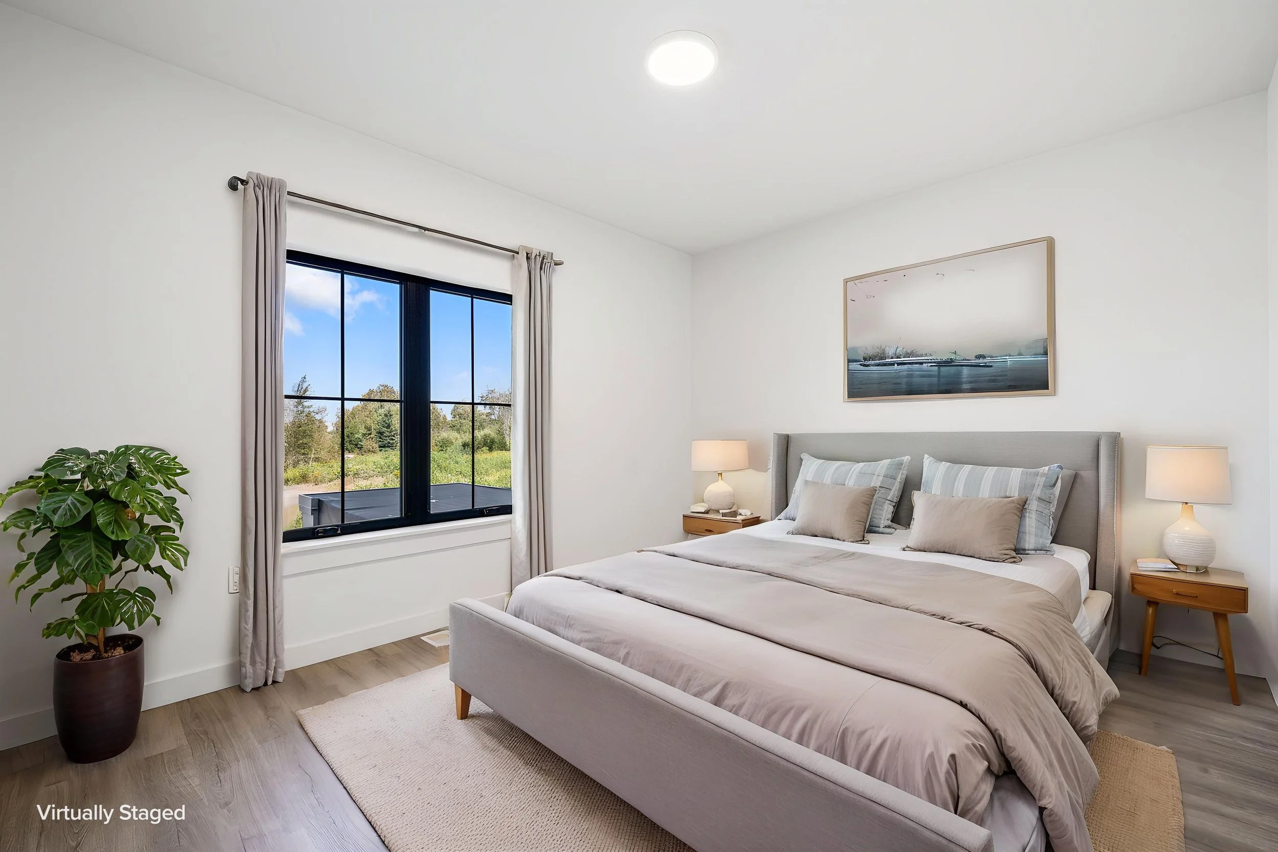 A bedroom with white walls, a large window with beige curtains, a bed with gray and beige bedding. The Residences at North Harbor on Lake Superior in Marquette Michigan.