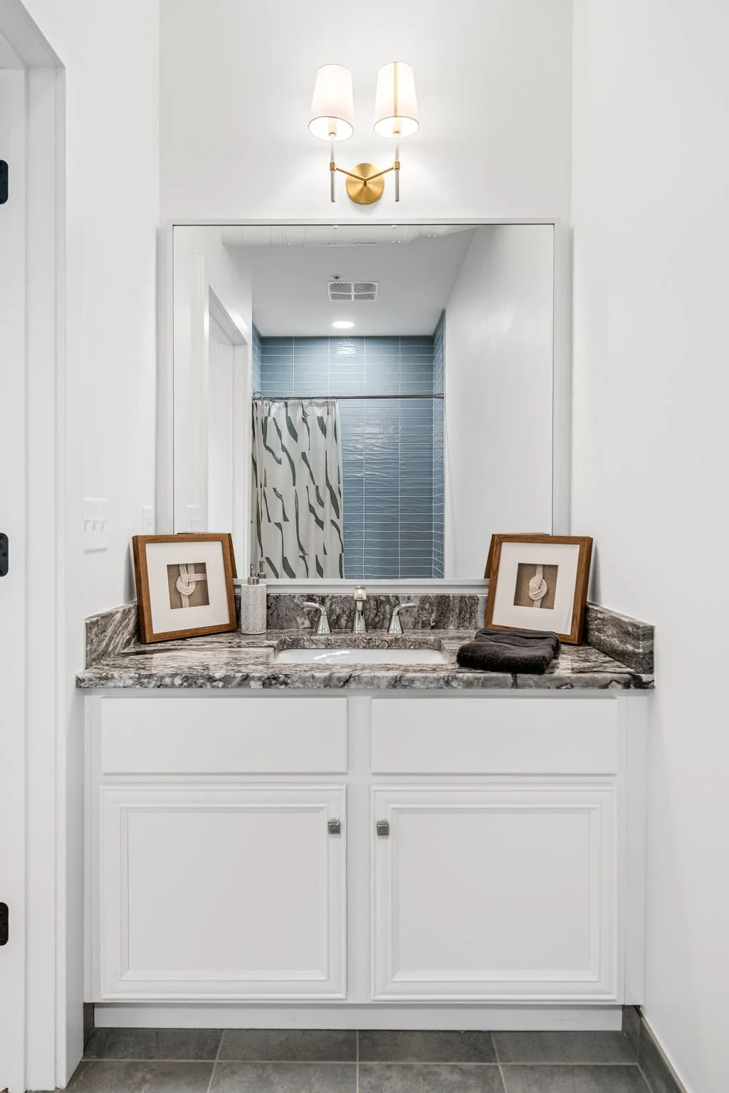 Bathroom vanity with a large mirror, two framed nautical artworks, a soap dispenser, and a folded towel. The Residences at North Harbor on Lake Superior in Marquette Michigan.