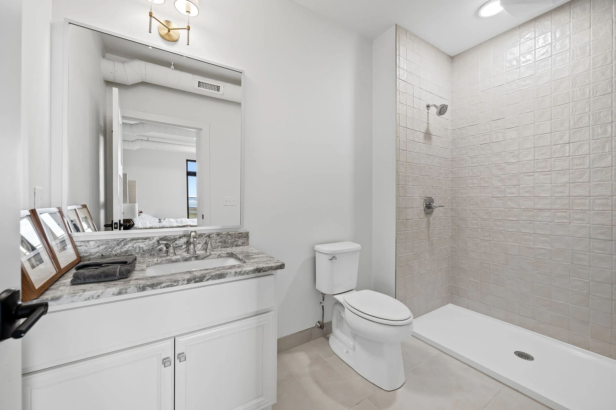 A modern bathroom featuring a white toilet, a vanity with a marble countertop, a mirror, and a walk-in shower with beige subway tiles and a showerhead. The Residences at North Harbor on Lake Superior in Marquette Michigan.