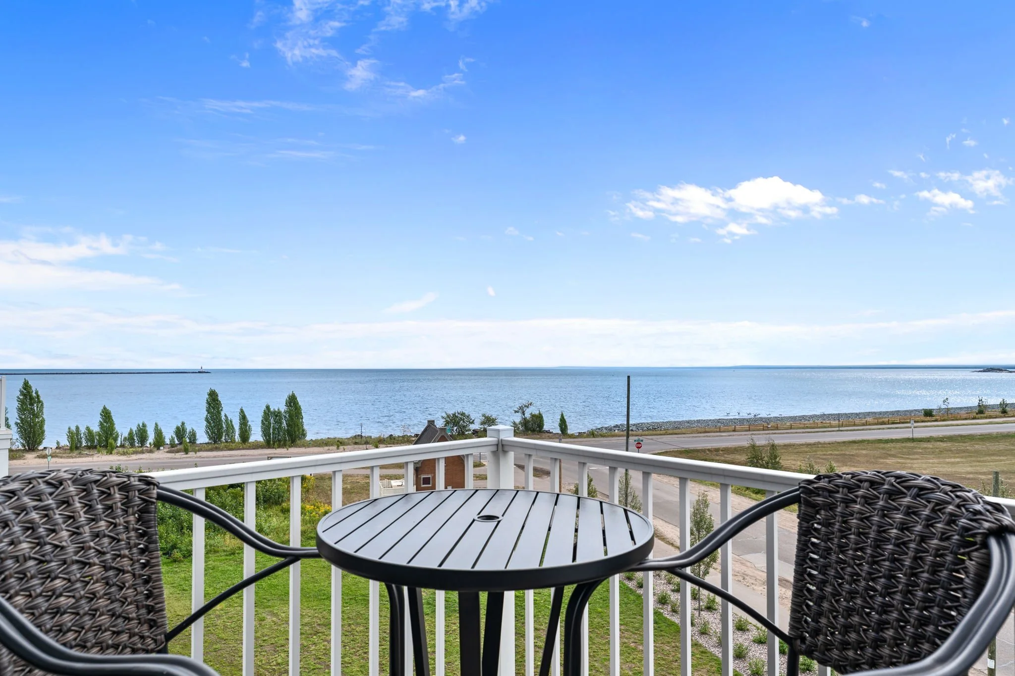 A balcony with a round table and two wicker chairs overlooking Lake Superior in Marquette Michigan, The Residences at North Harbor.
