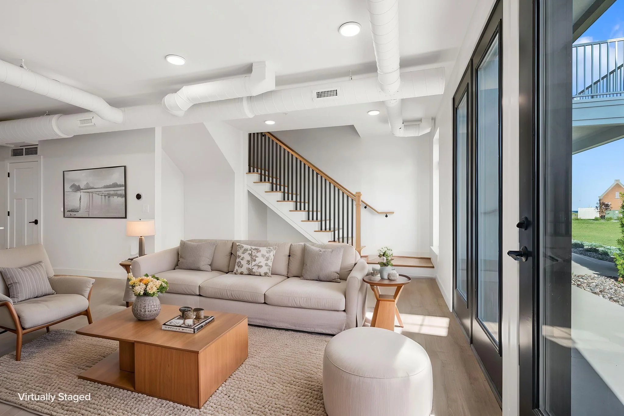 Modern living room with beige sofas, a wooden coffee table, and large glass sliding doors leading outside. The Residences at North Harbor on Lake Superior in Marquette Michigan.