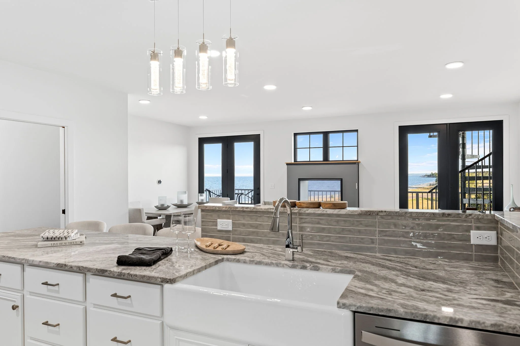 Modern kitchen with a marble island, white cabinets, and large windows showing a water view outside. The Residences at North Harbor on Lake Superior in Marquette Michigan.