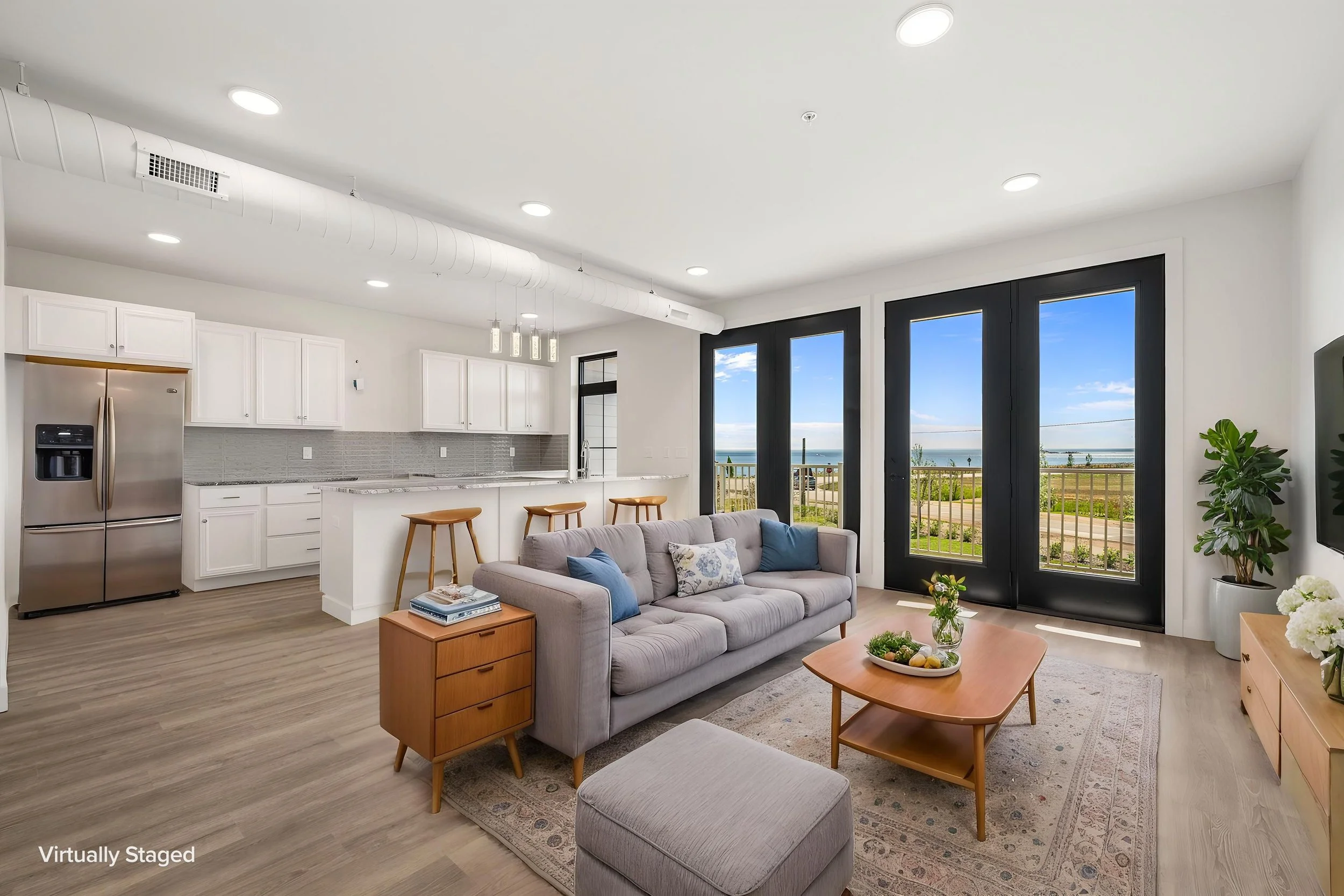 Living room with large windows showing a view of the outdoors, a sofa with cushions, a wooden coffee table, and a potted plant. The Residences at North Harbor on Lake Superior in Marquette Michigan.