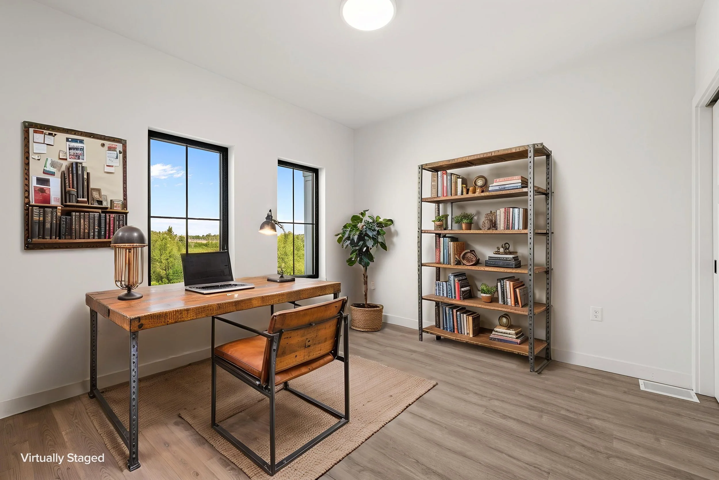 A home office with a wooden desk, black metal frame, and two chairs. There is a laptop and a lamp on the desk. Two windows behind the desk reveal a green landscape. The Residences at North Harbor on Lake Superior in Marquette Michigan.