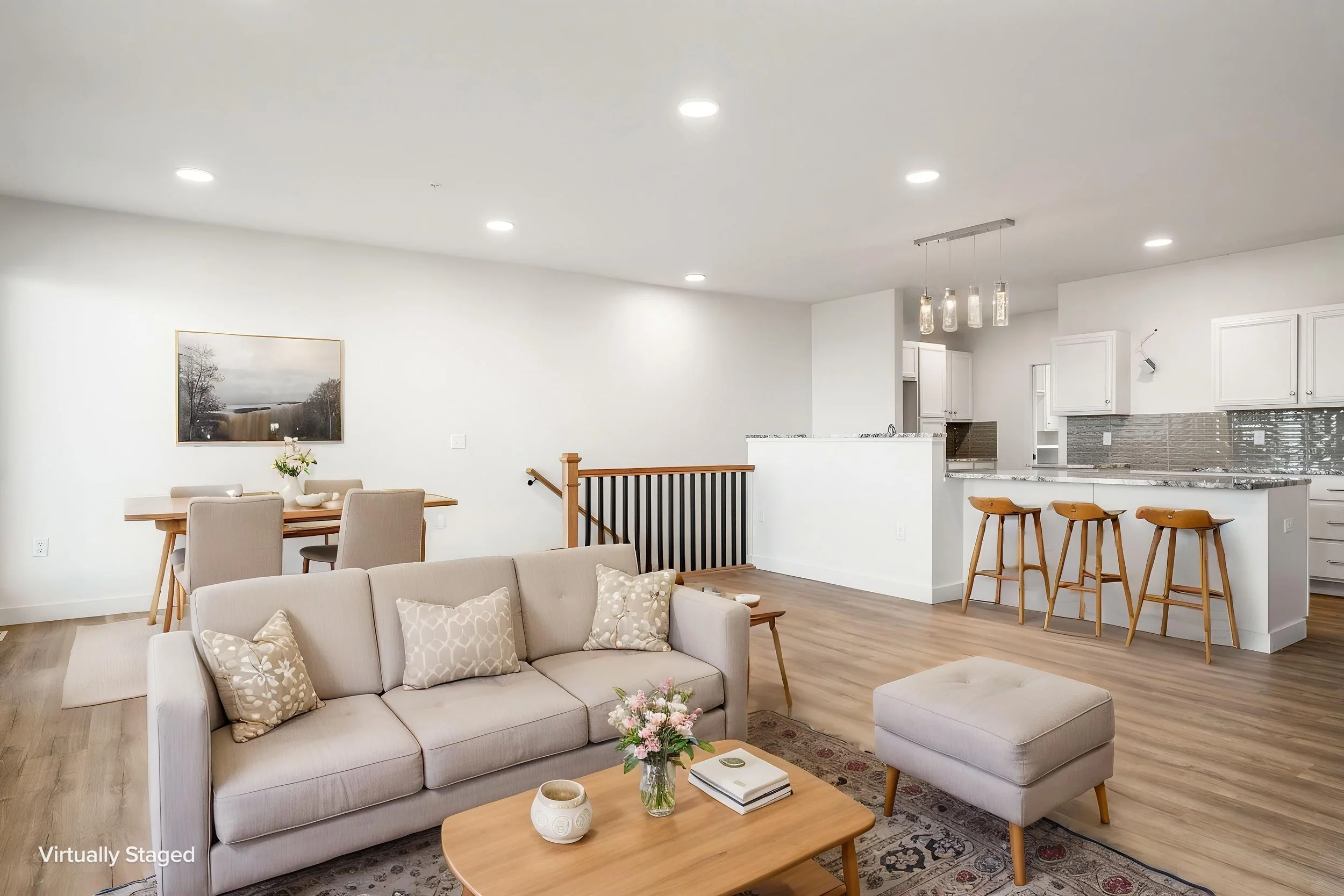 Open concept living room with beige sofa, throw pillows, and coffee table with flowers, adjacent to a dining area with a wooden table. The Residences at North Harbor on Lake Superior in Marquette Michigan.