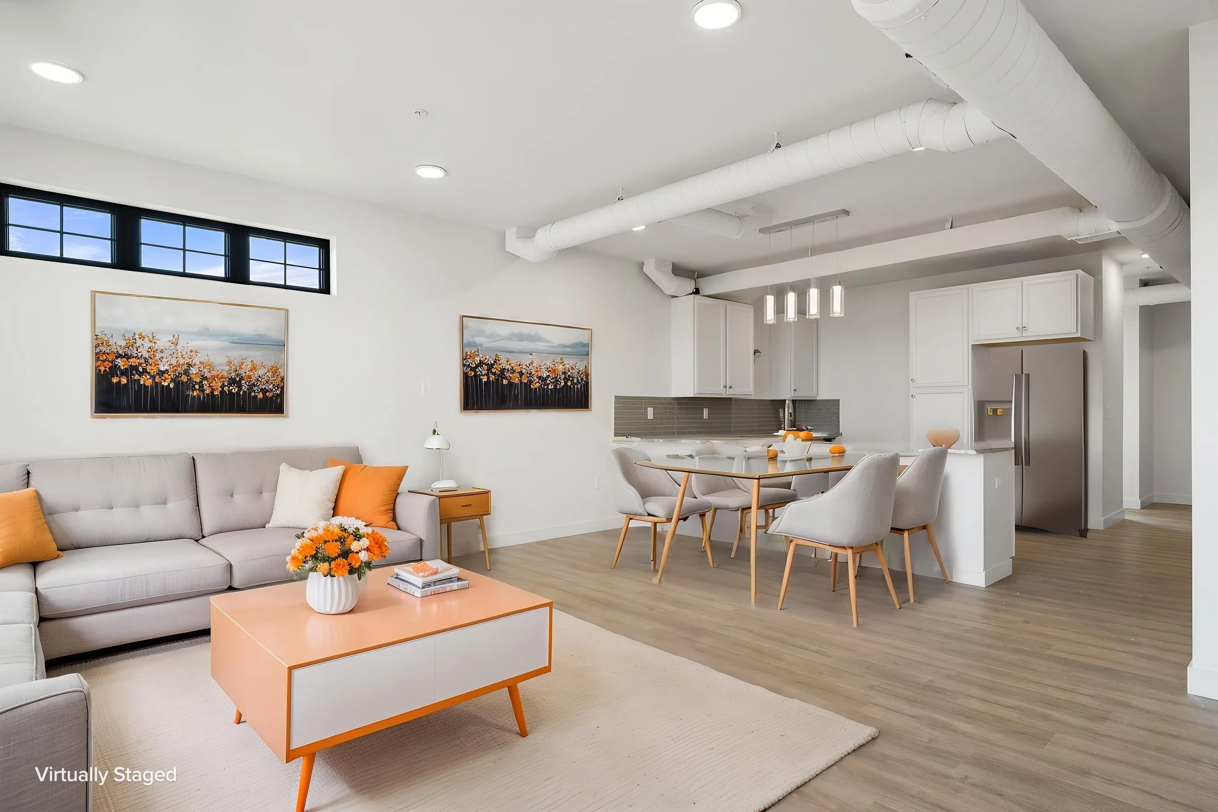 Open-concept living area with white walls, wooden flooring, white sofa with orange and white pillows,. The Residences at North Harbor on Lake Superior in Marquette Michigan.