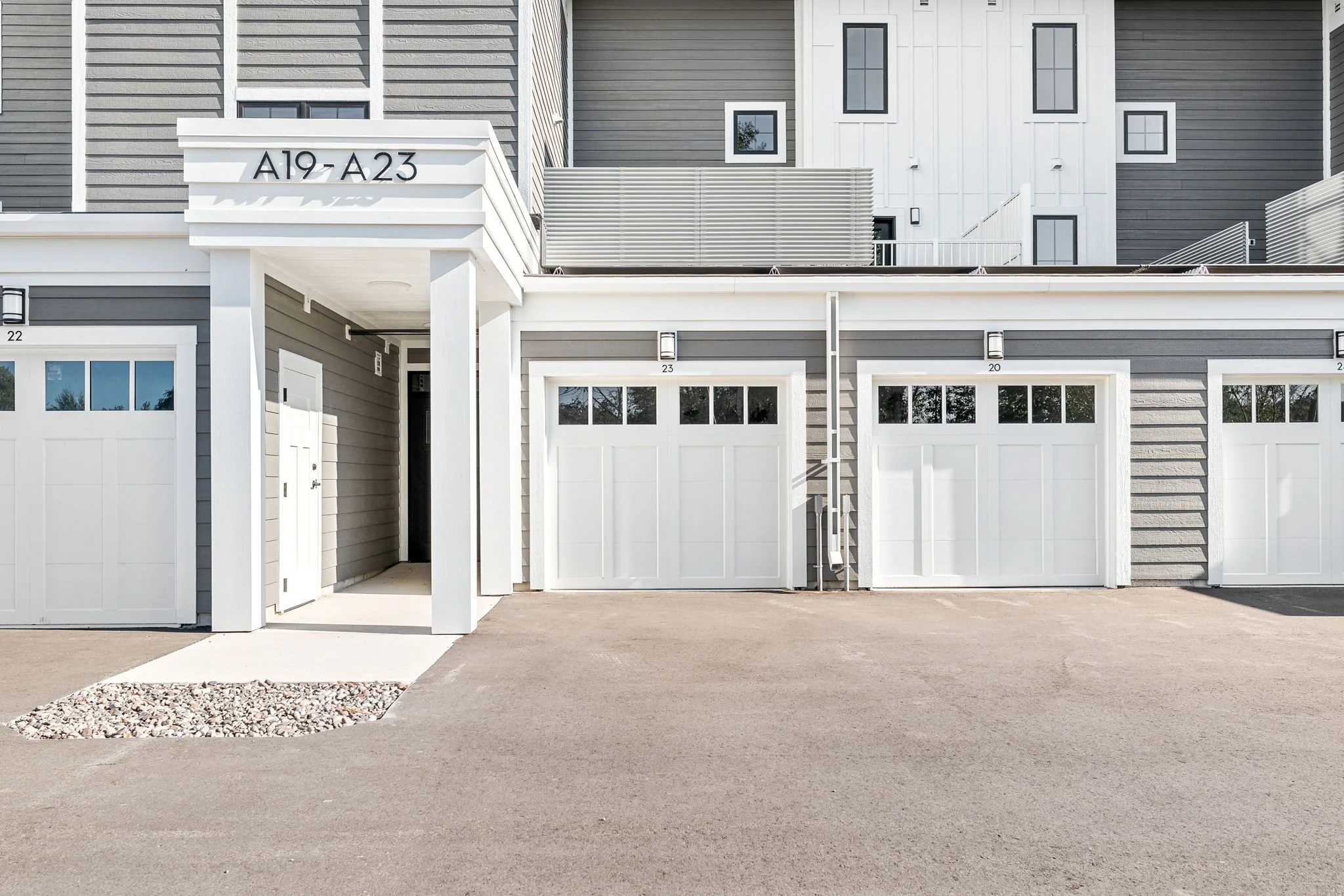 A row of modern townhouses with gray and white siding, garage doors, and small porch areas. The Residences at North Harbor on Lake Superior in Marquette Michigan.