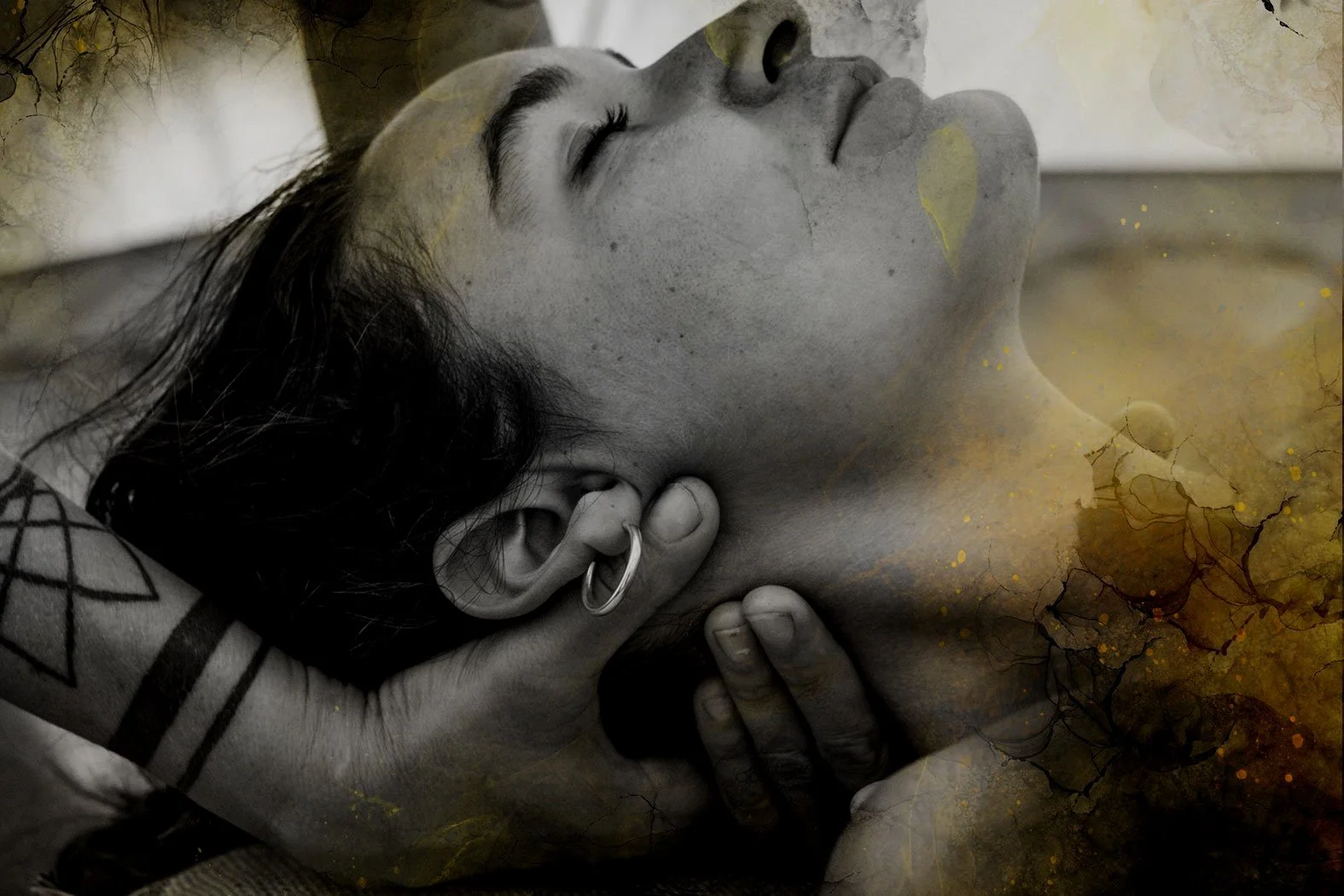 A person with dark hair and tattoos, lying down with eyes closed, resting their head on a hand, with an artistic overlay of cracked, textured watercolor effects.