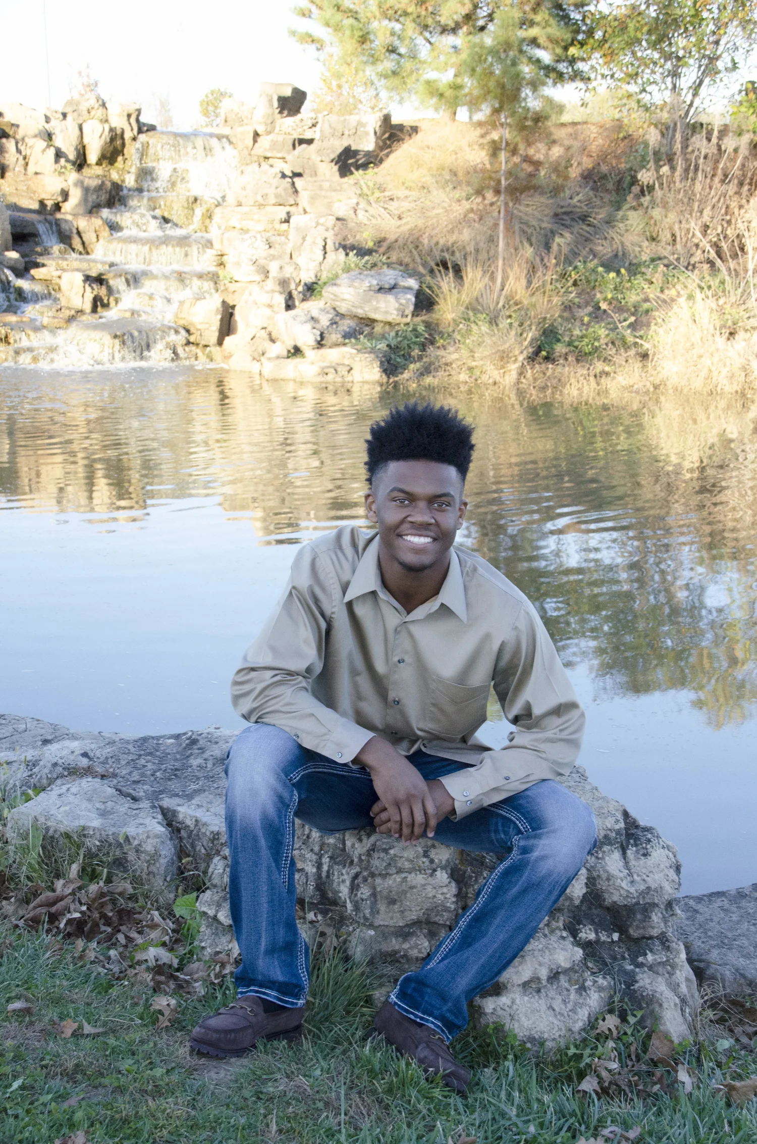 A smiling young man seated beside a pond