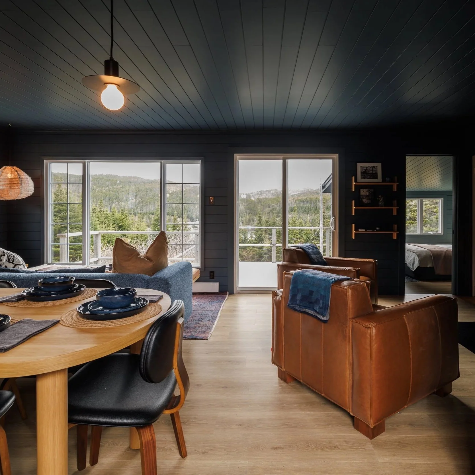 Kitchen corner with dark blue shiplap walls, a window with a view of trees, a framed black-and-white boat photograph, hanging pots and pans, a coffee maker, cups, and kitchen appliances.
