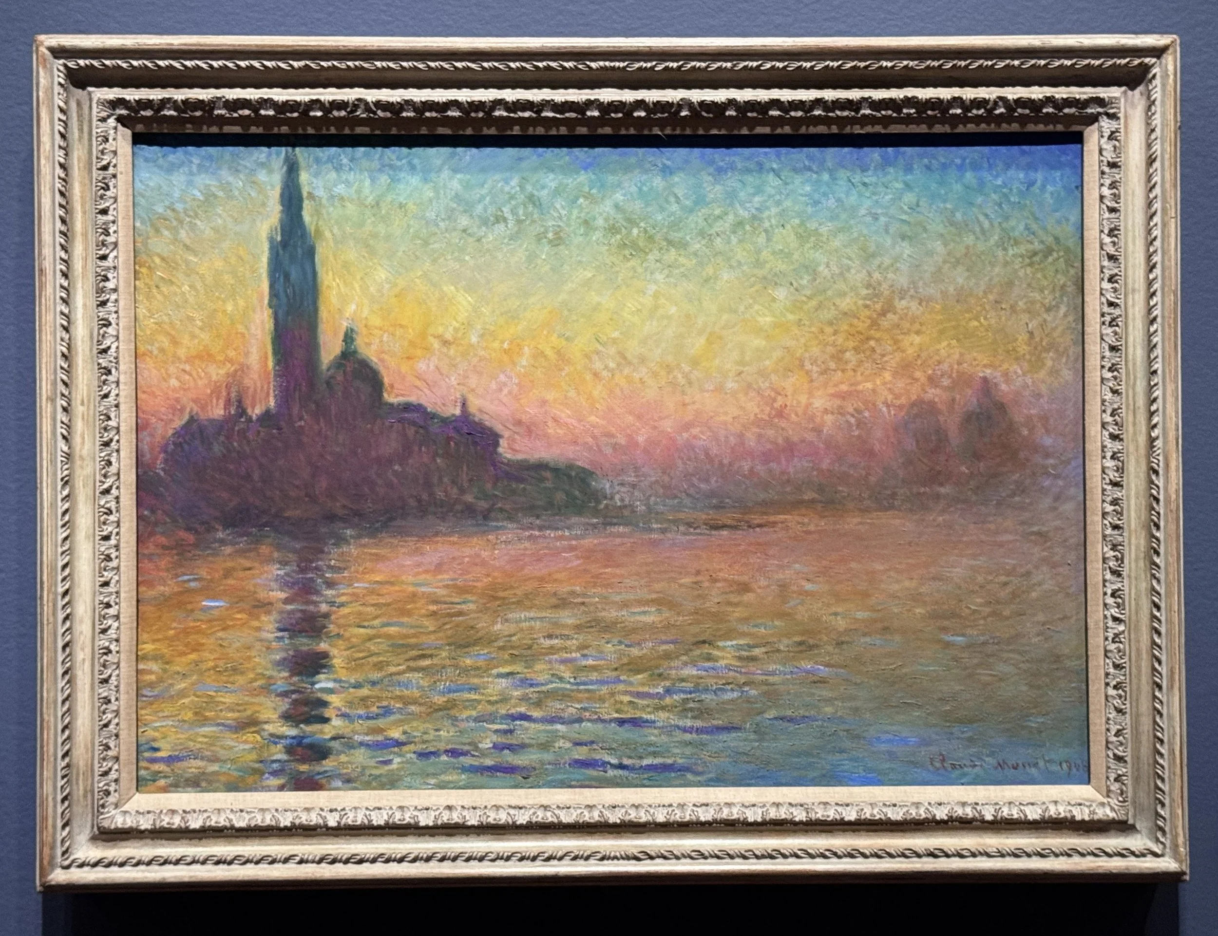 Monet's painting of San Giorgio Maggiore shows the iconic landmark silhouetted against the vivid violet, blue, gold and rose sky colors, which are then reflecting across the calm surface of the water.