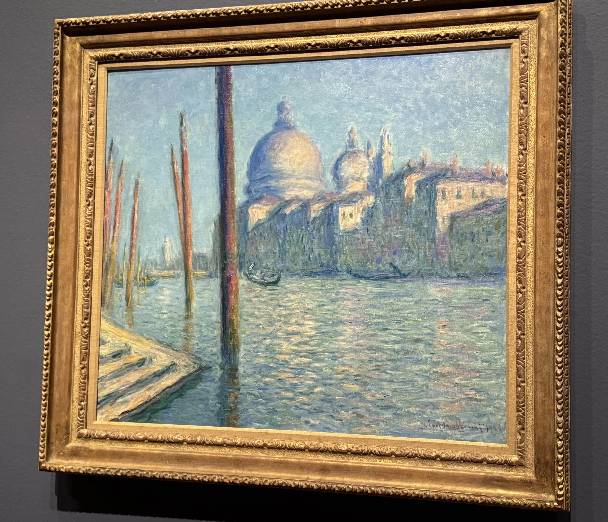 Claude Monet painting of the grand canal Venice, with predominant blues and greens. Several gondolas are on the water, and Santa Maria della Salute church is across the canal.