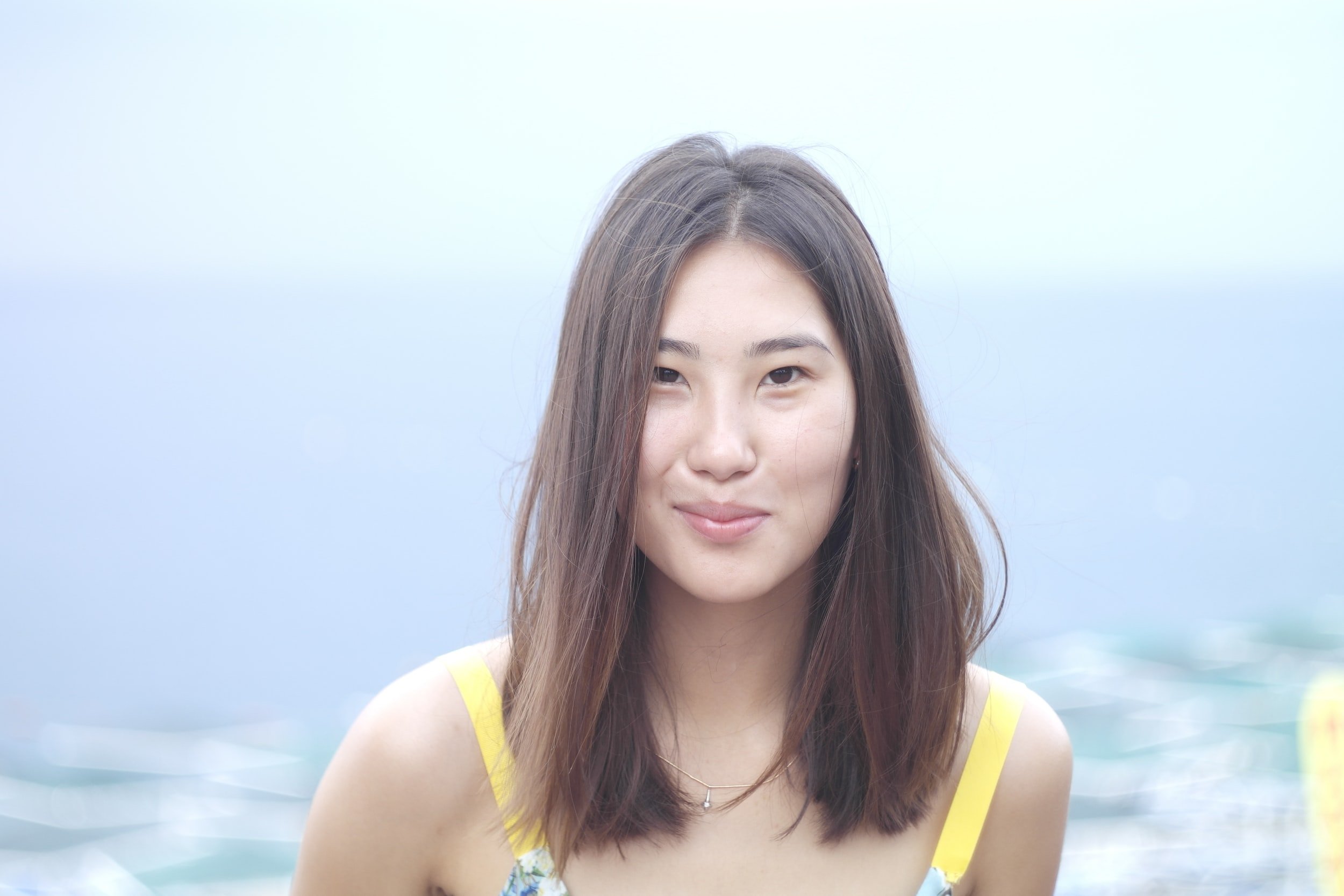Young woman with long hair smiling in front of a blurred outdoor background.