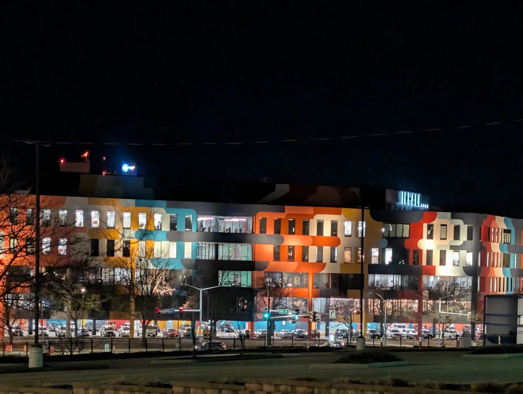 Mainframe Studios exterior, with the cityscape at dusk with tall buildings, a colorful mural on a building, and a parking lot with cars.