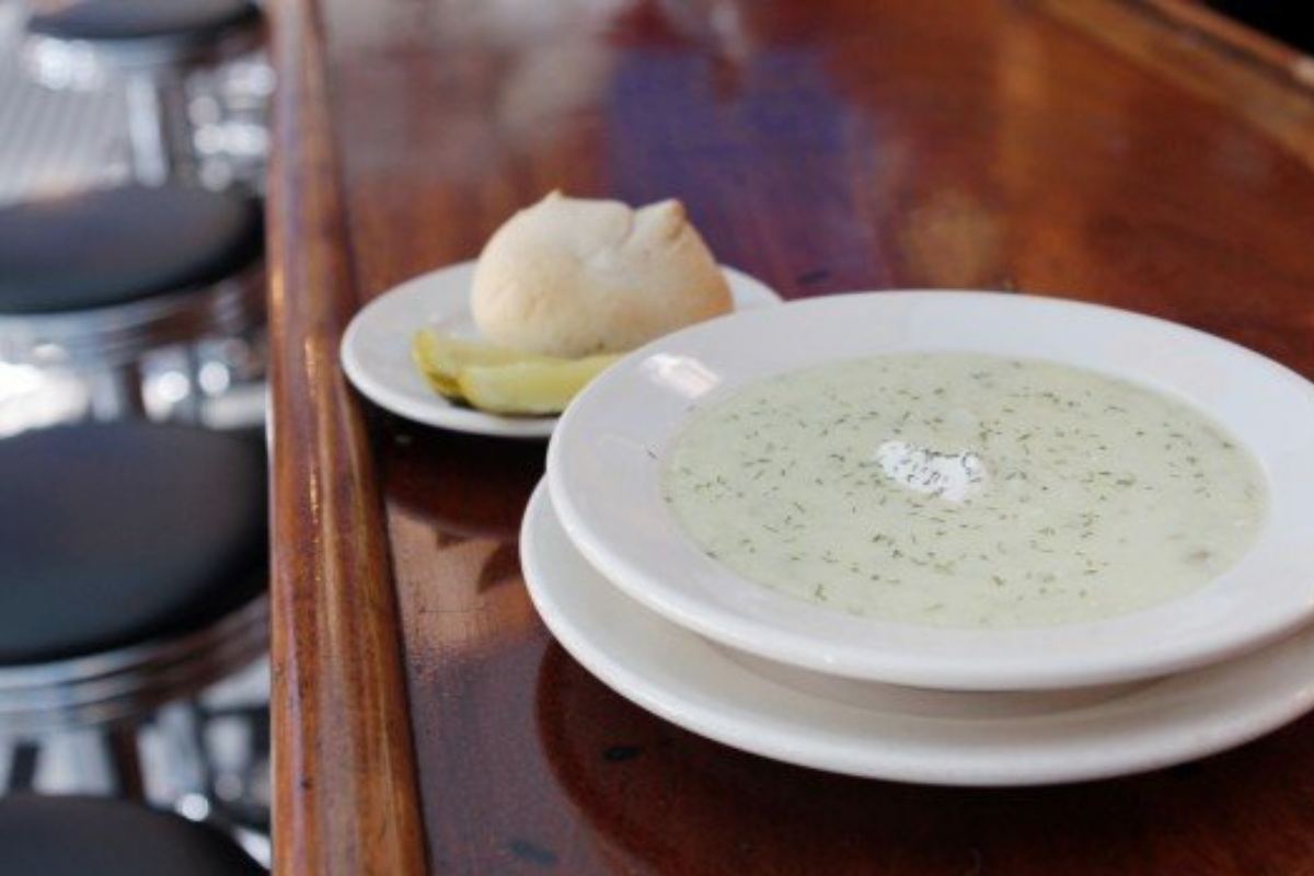 A bowl of pickle soup sits on the bar at The Fountain on Locust next to rolls and butter.