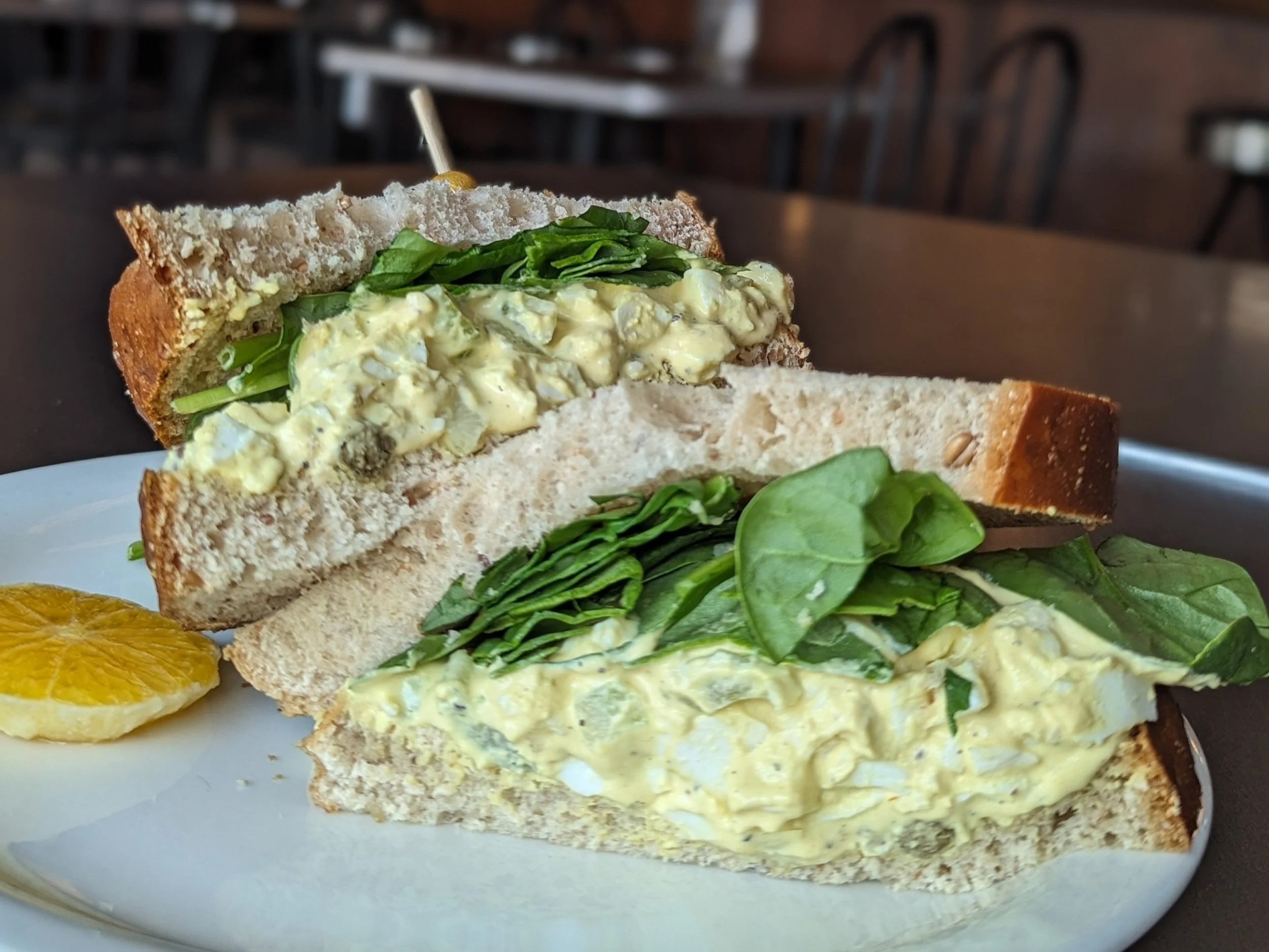 Our Classic Egg Salad Sandwich the High Hat served on a plate with an orange slice