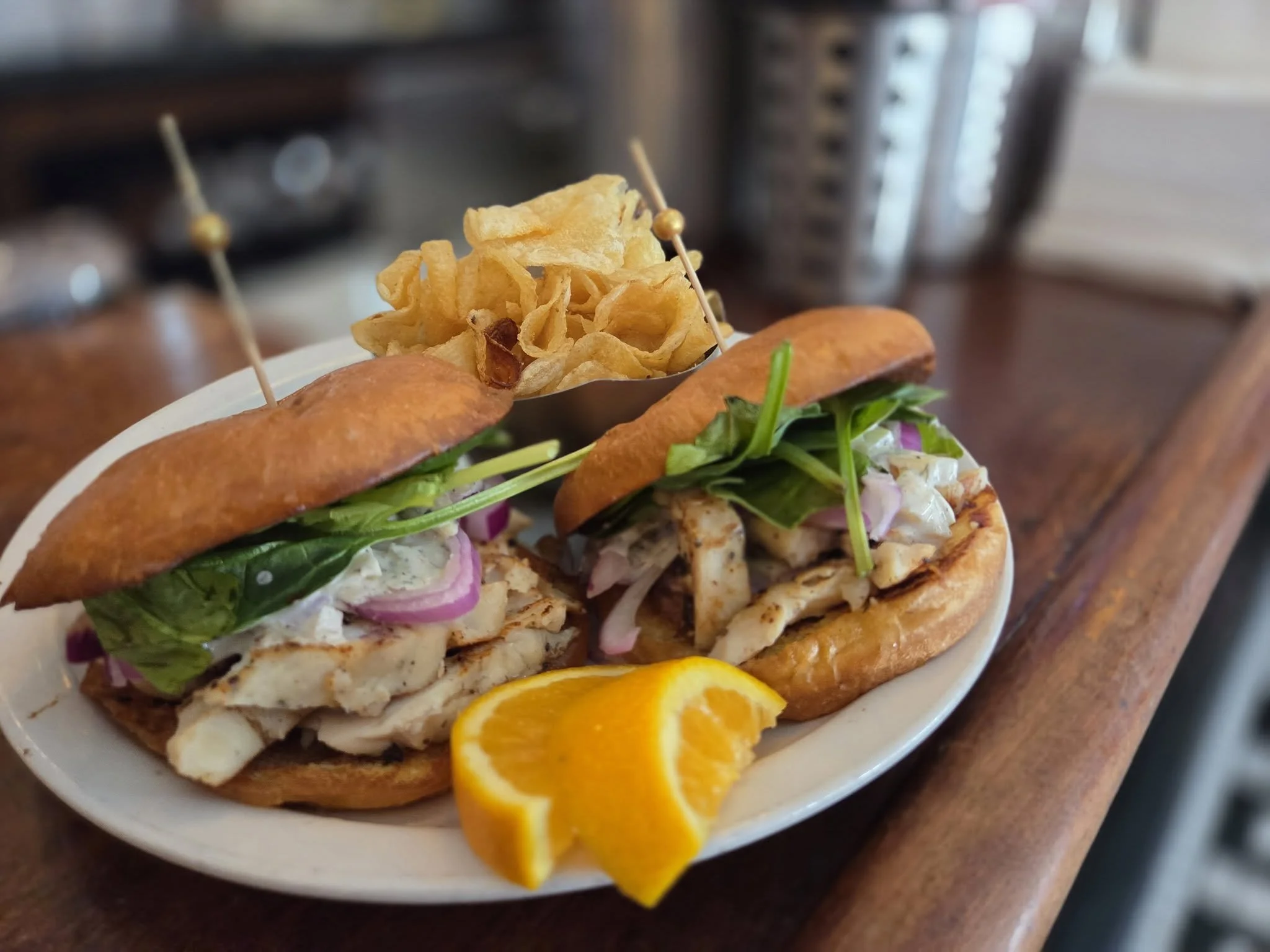 Greek Chicken Slider sandwiches sit on a plate next to kettle chips and orange slices at The Fountain on Locust in Midtown St. Louis