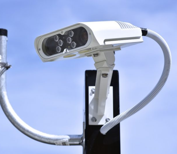 Genetec AutoVu SharpV License plate recognition. A security camera mounted on a pole against a blue sky.